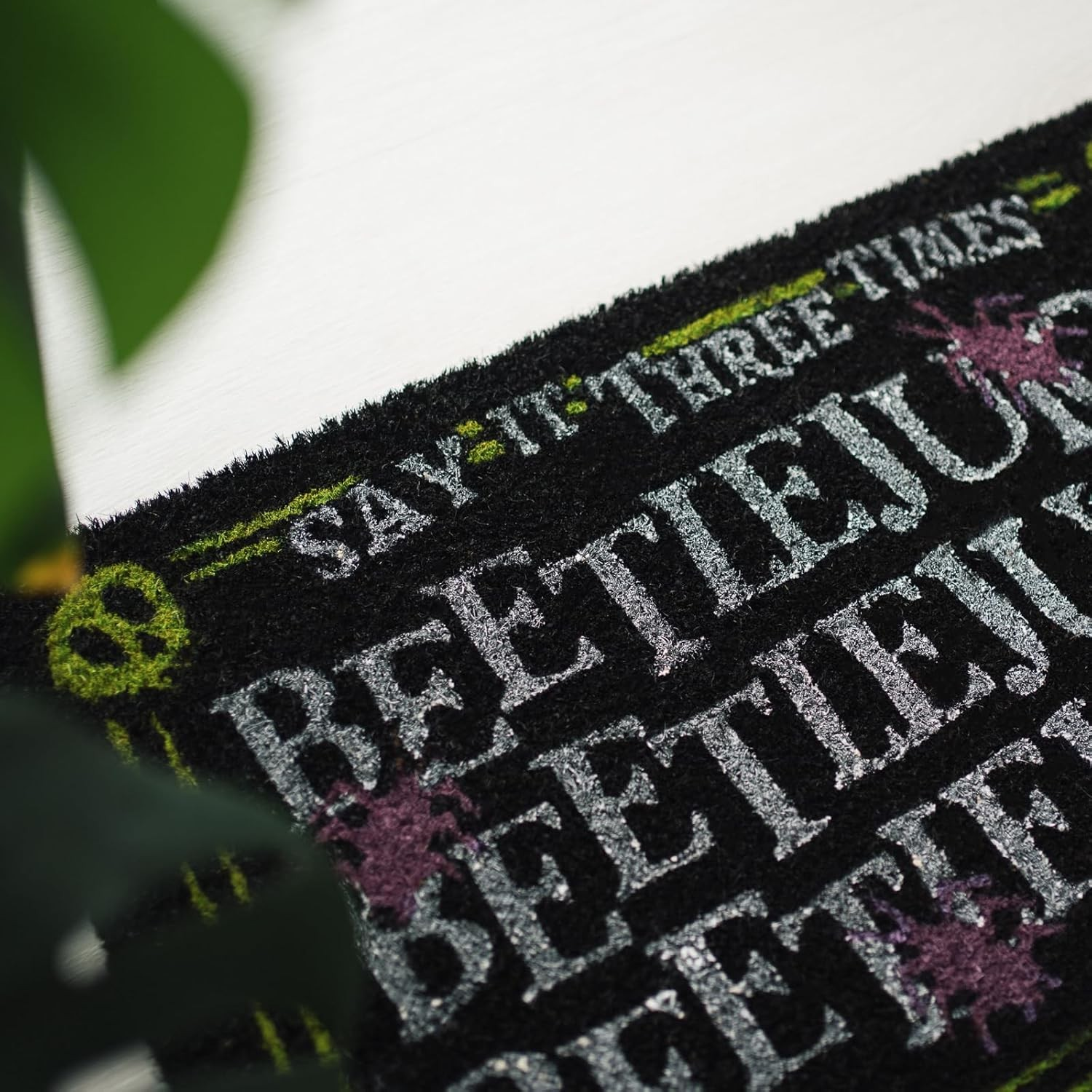 Felpudo negro con texto en blanco y detalles en verde y morado.