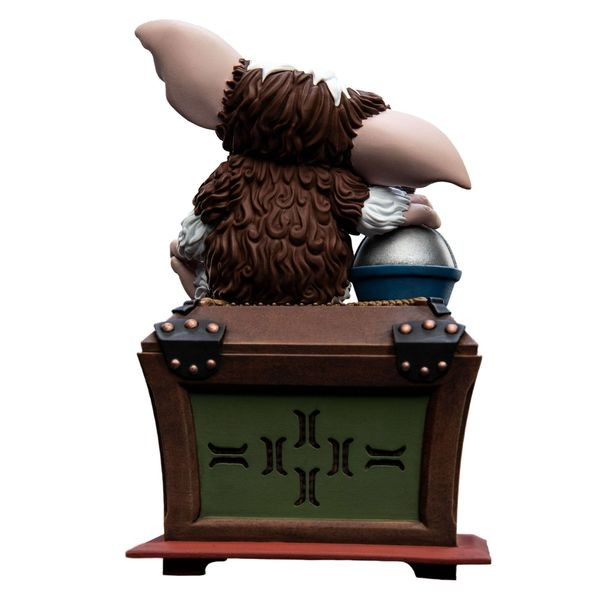 Rückansicht einer flauschigen Gremlin-Figur mit großen Ohren auf einer Holzkiste vor weißem Hintergrund.