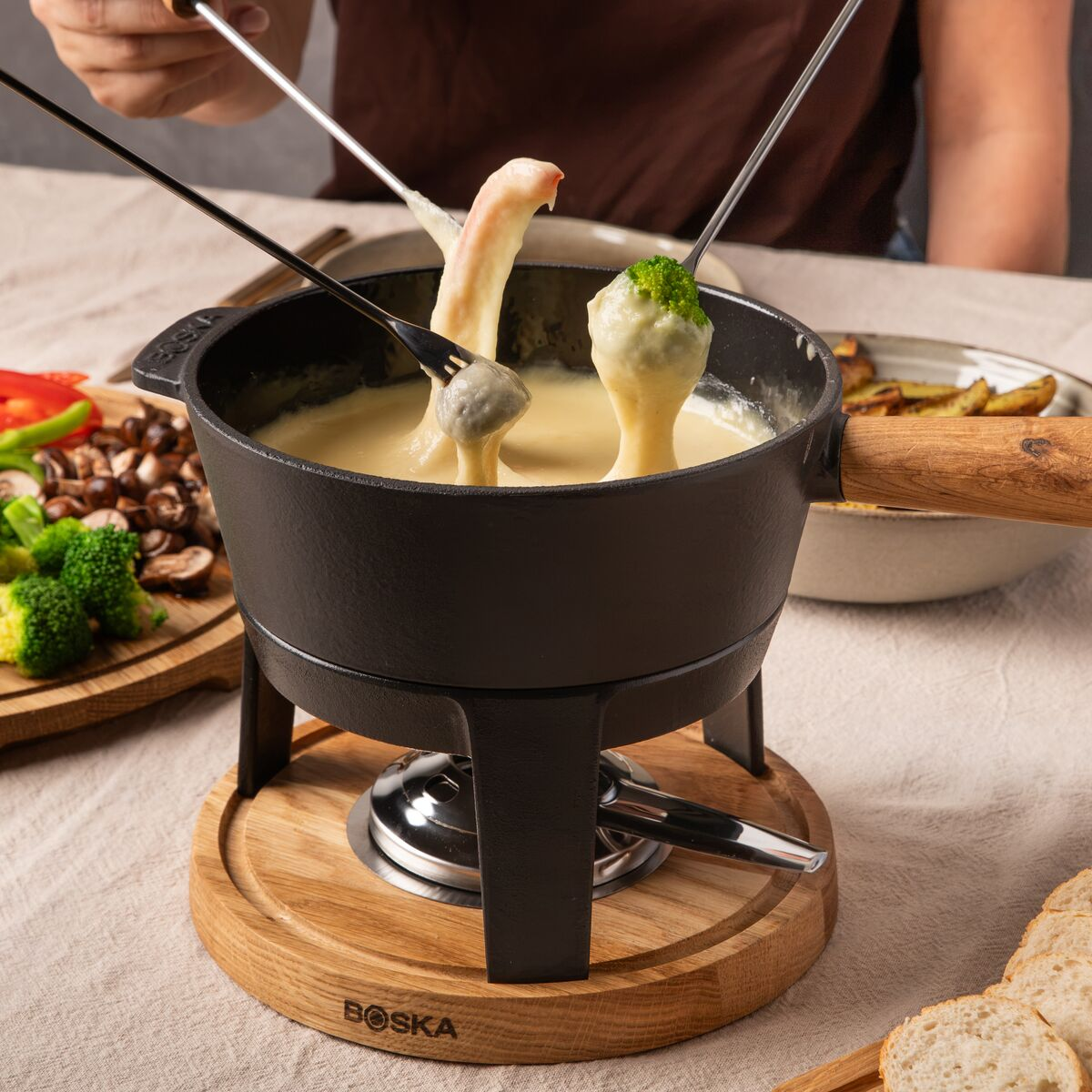 Menschen tauchen Brokkoli und Brot mit langen Gabeln in einen Fonduetopf voller geschmolzenem Käse.