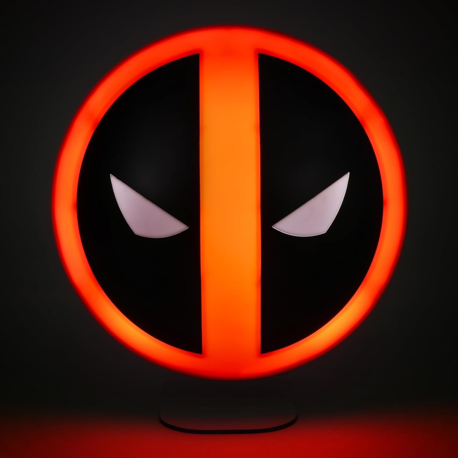 Eine leuchtende Deadpool-Logo-Lampe mit rotem Rand und weißen Augen auf schwarzem Grund vor dunklem Hintergrund.