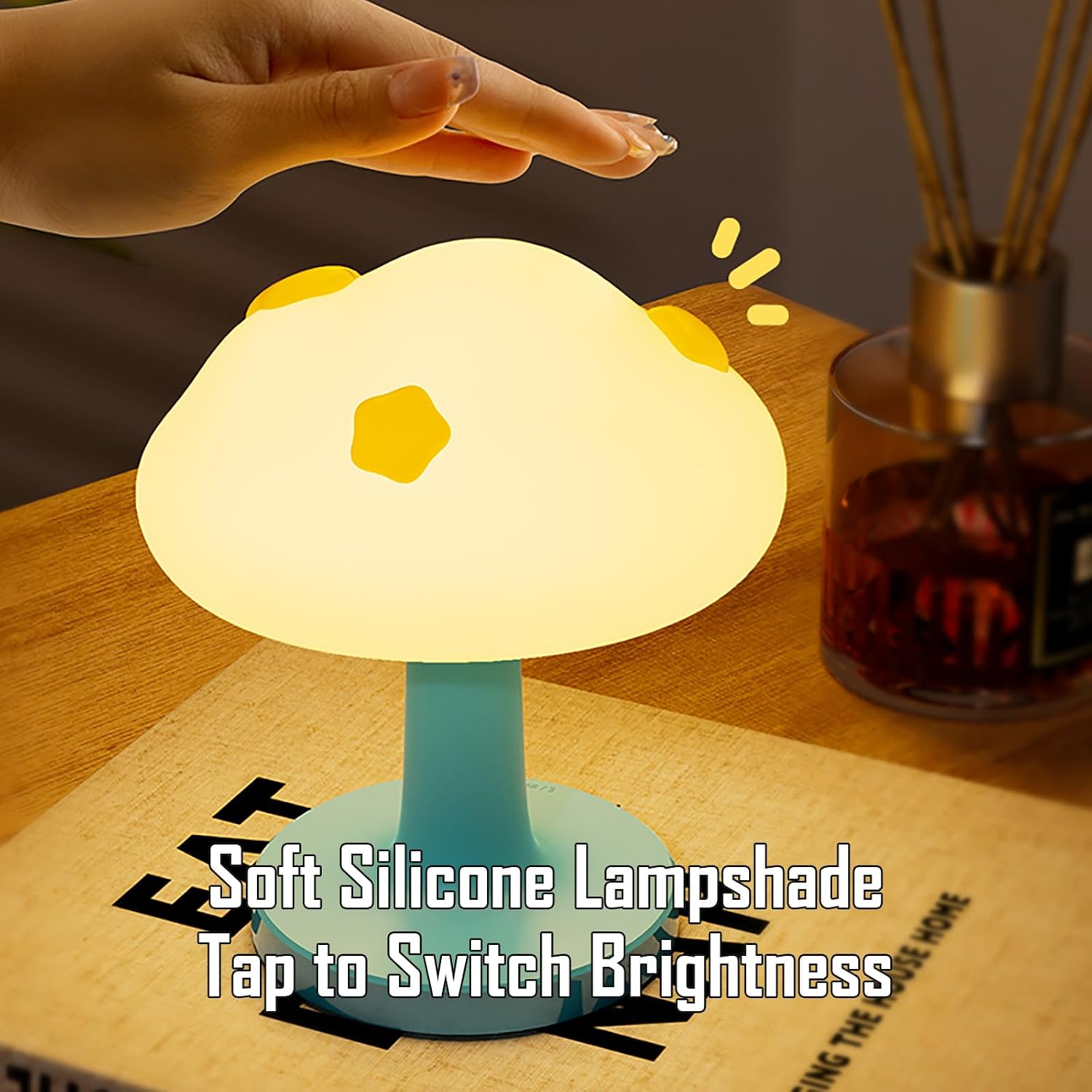 Eine Hand tippt auf eine weiche, gelbe Pilzlampe mit blauem Ständer auf einem Holztisch.