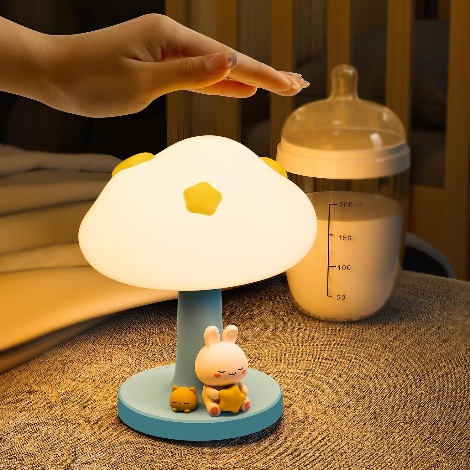 Hand berührt eine niedliche Wolken-Nachtlampe mit Kaninchenfigur und Babyflasche im Hintergrund.