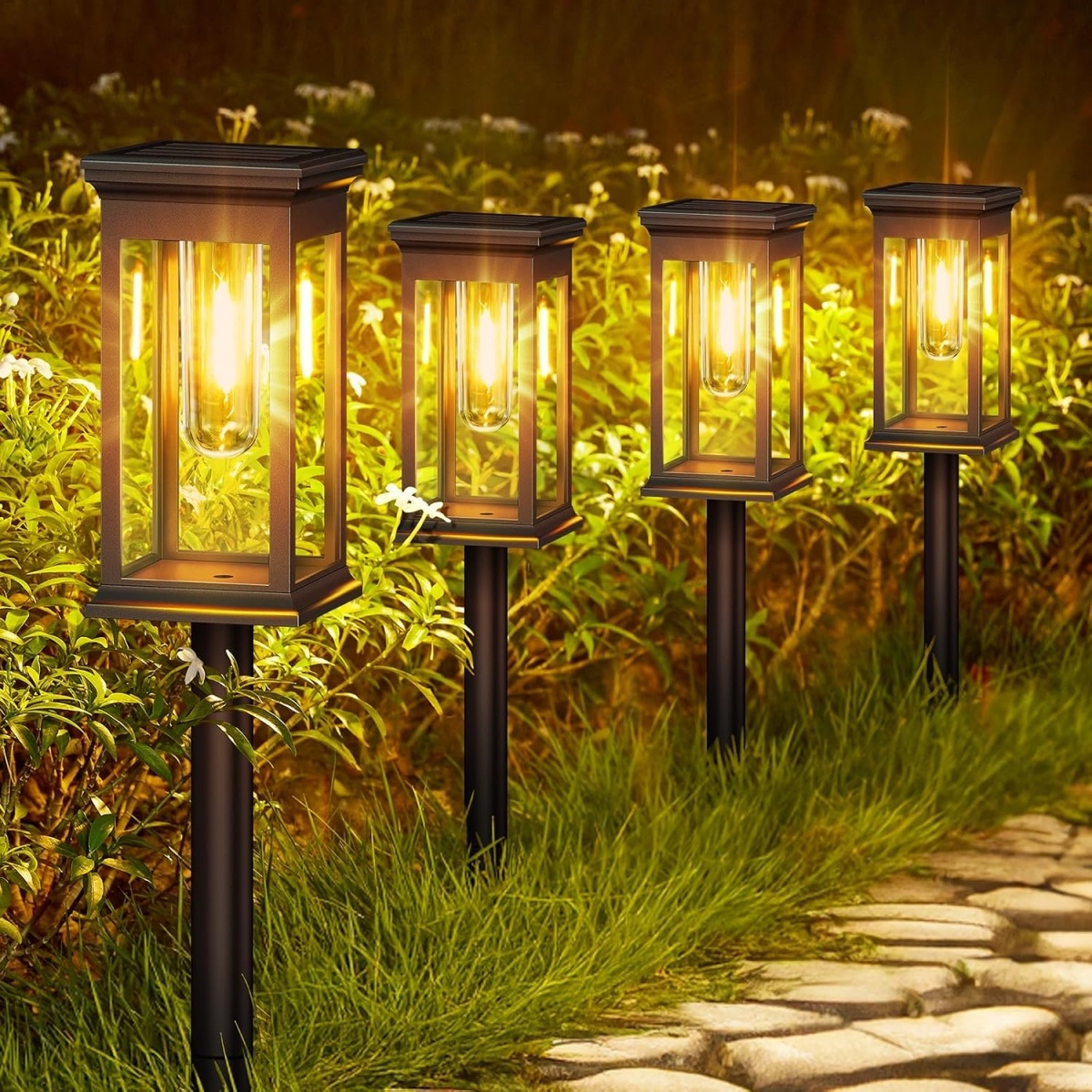 Vier solarbetriebene Gartenlampen leuchten entlang eines Steinwegs im Garten.