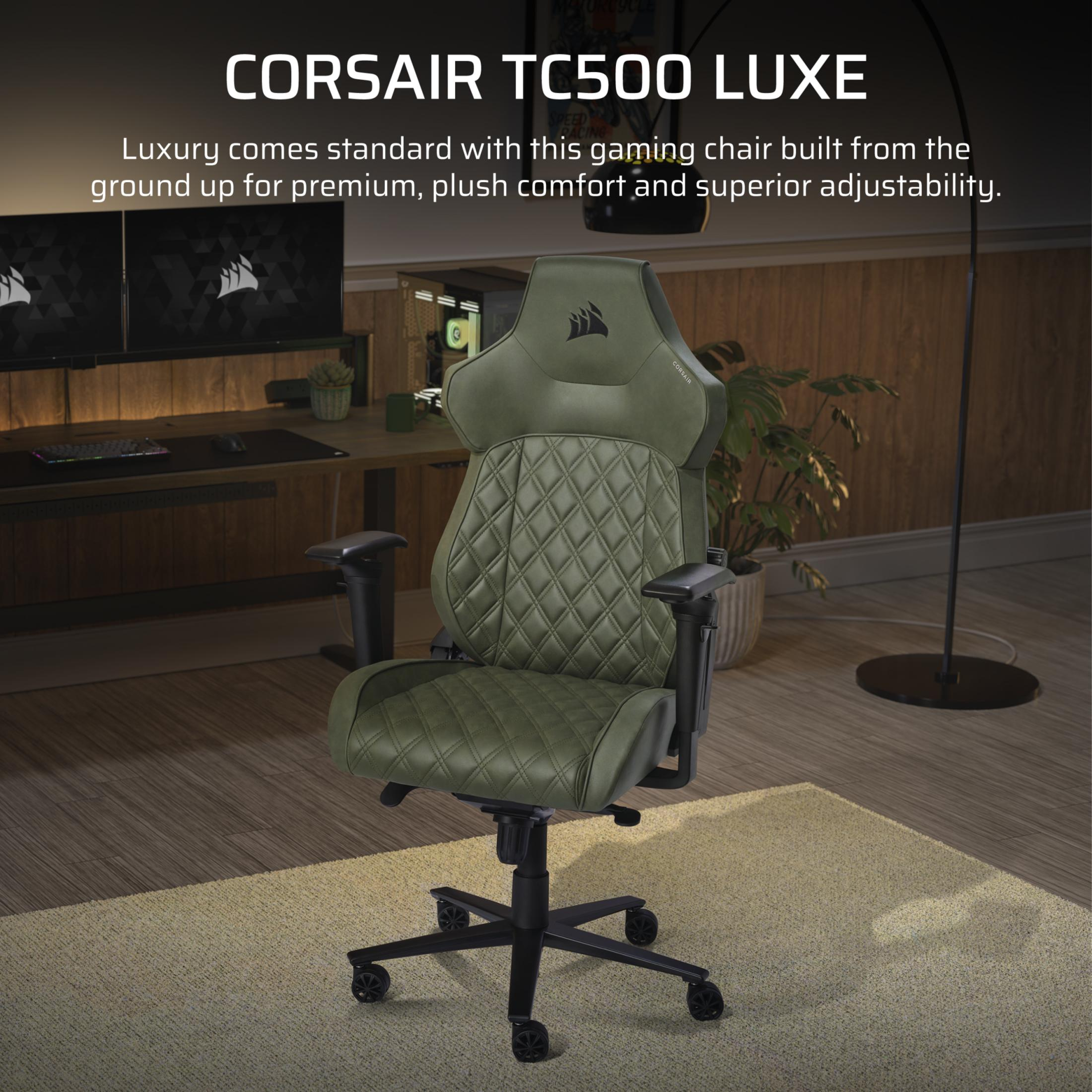 Ein olivgrüner Gaming-Stuhl steht auf einem Teppich in einem modernen Zimmer mit Holztisch und Monitoren.