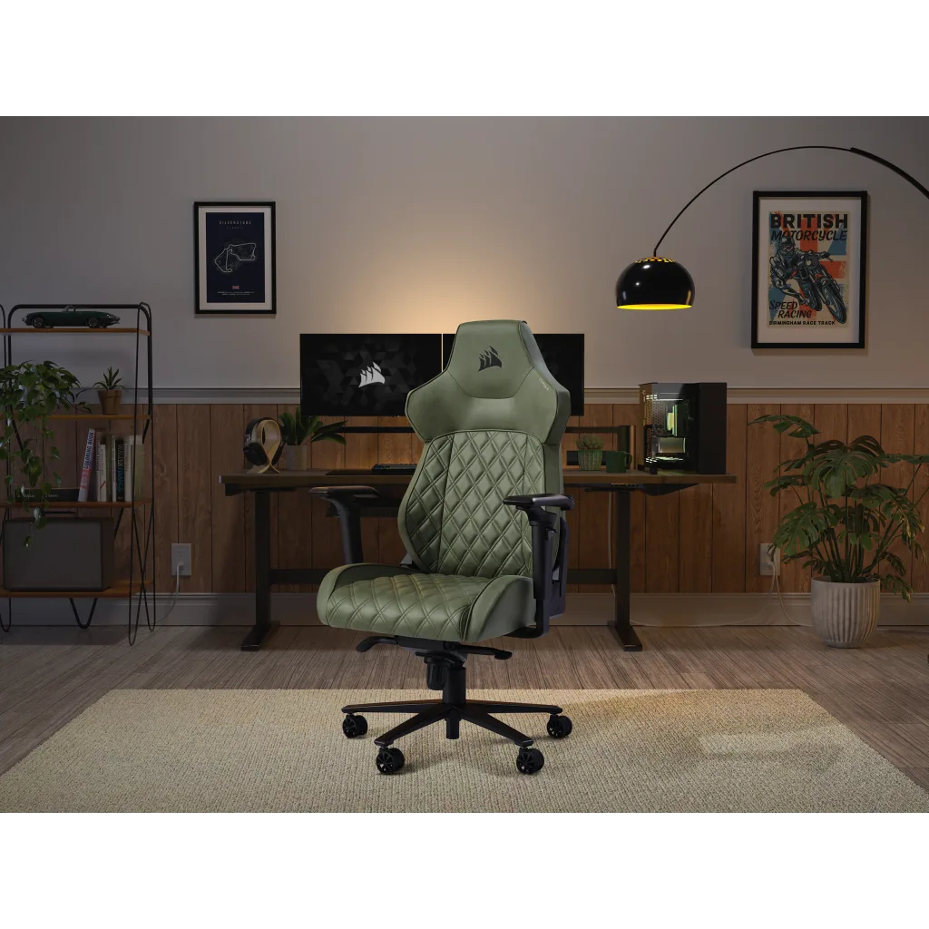 Ein grüner Gaming-Stuhl steht im Vordergrund eines Arbeitszimmers mit Schreibtisch, Computern und Pflanzen.
