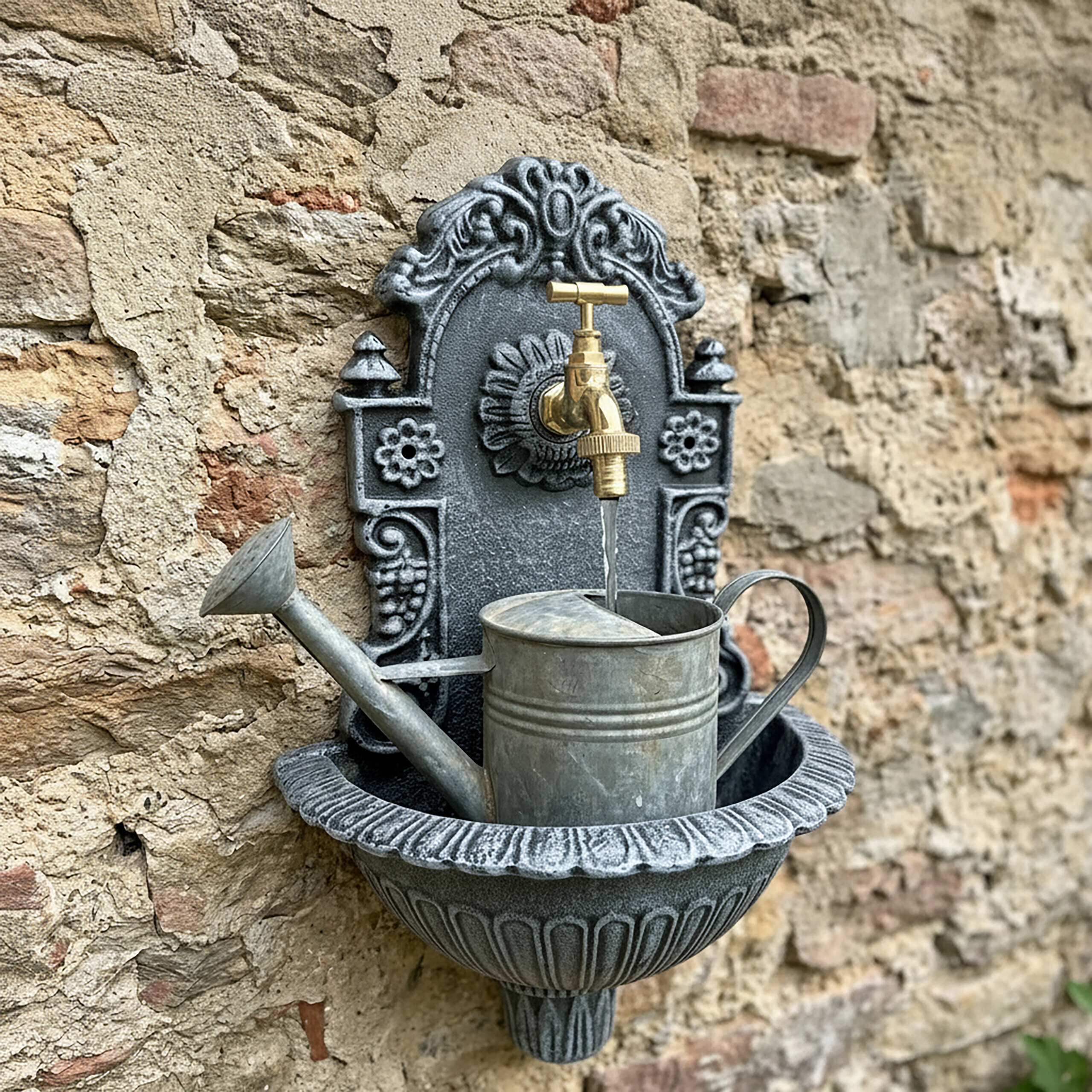 Ein grauer Wandbrunnen mit goldenem Wasserhahn und einer silbernen Gießkanne an einer alten Steinmauer.