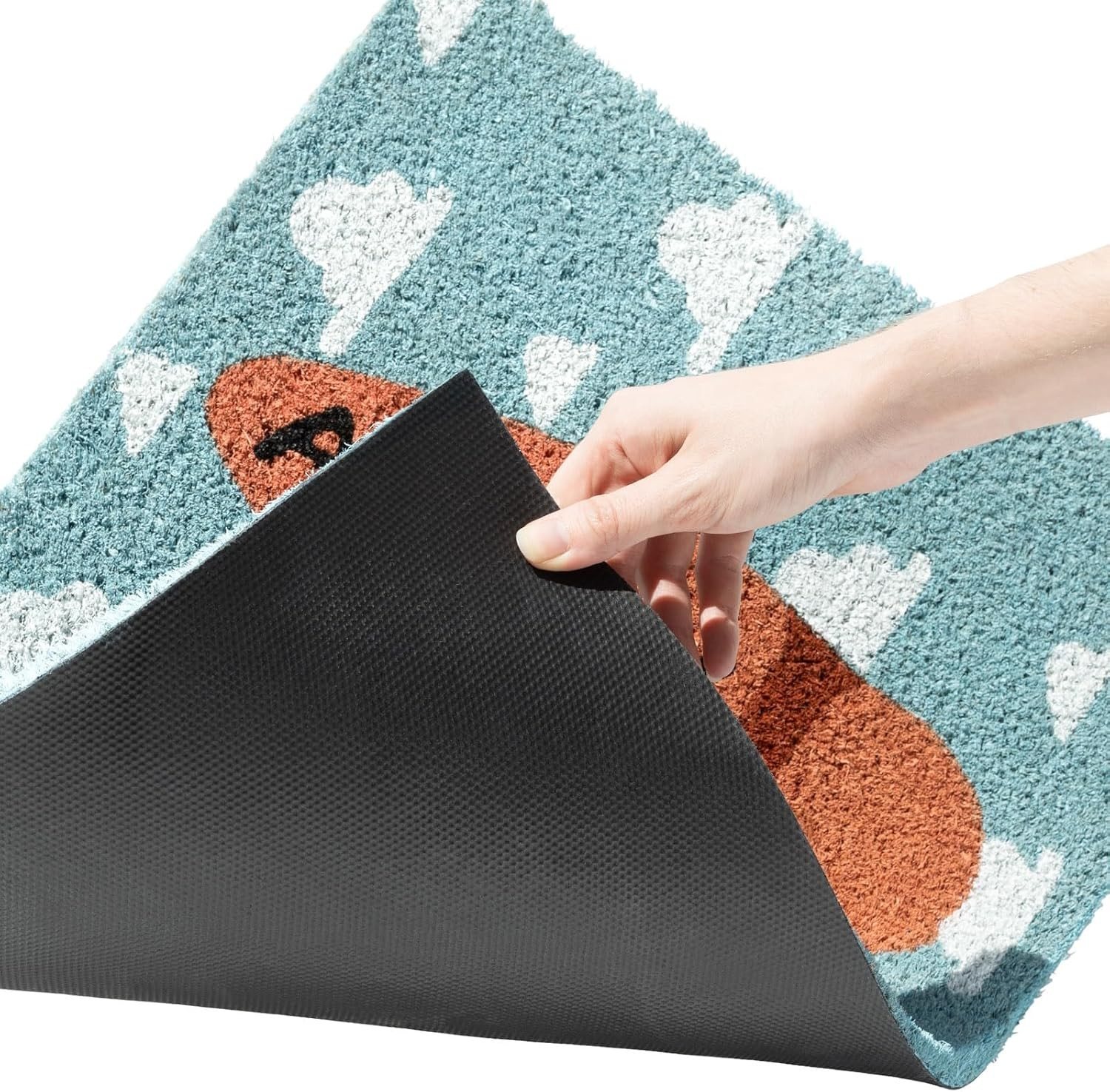 Una mano levanta una alfombra azul con nubes, mostrando su reverso negro antideslizante.