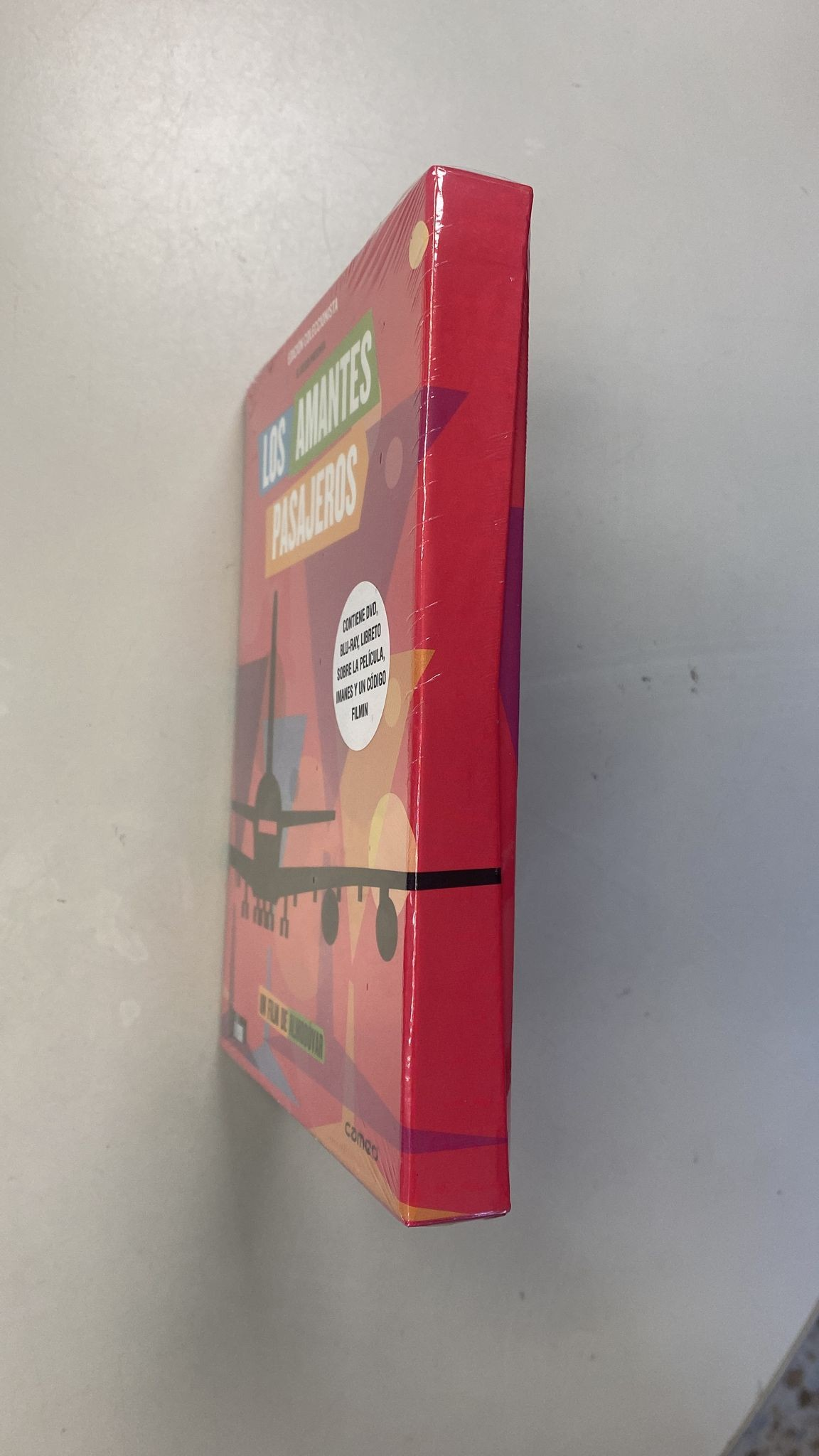 Una caja roja titulada Los Amantes Pasajeros sobre una superficie clara.
