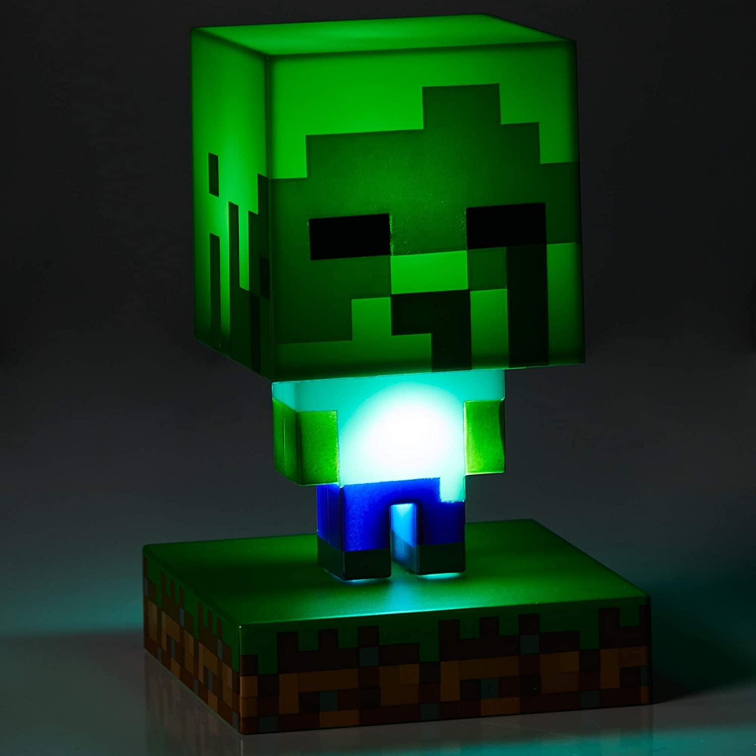 Eine grüne Minecraft Zombie Lampe leuchtet auf einem braunen und grünen Sockel in einem dunklen Raum.