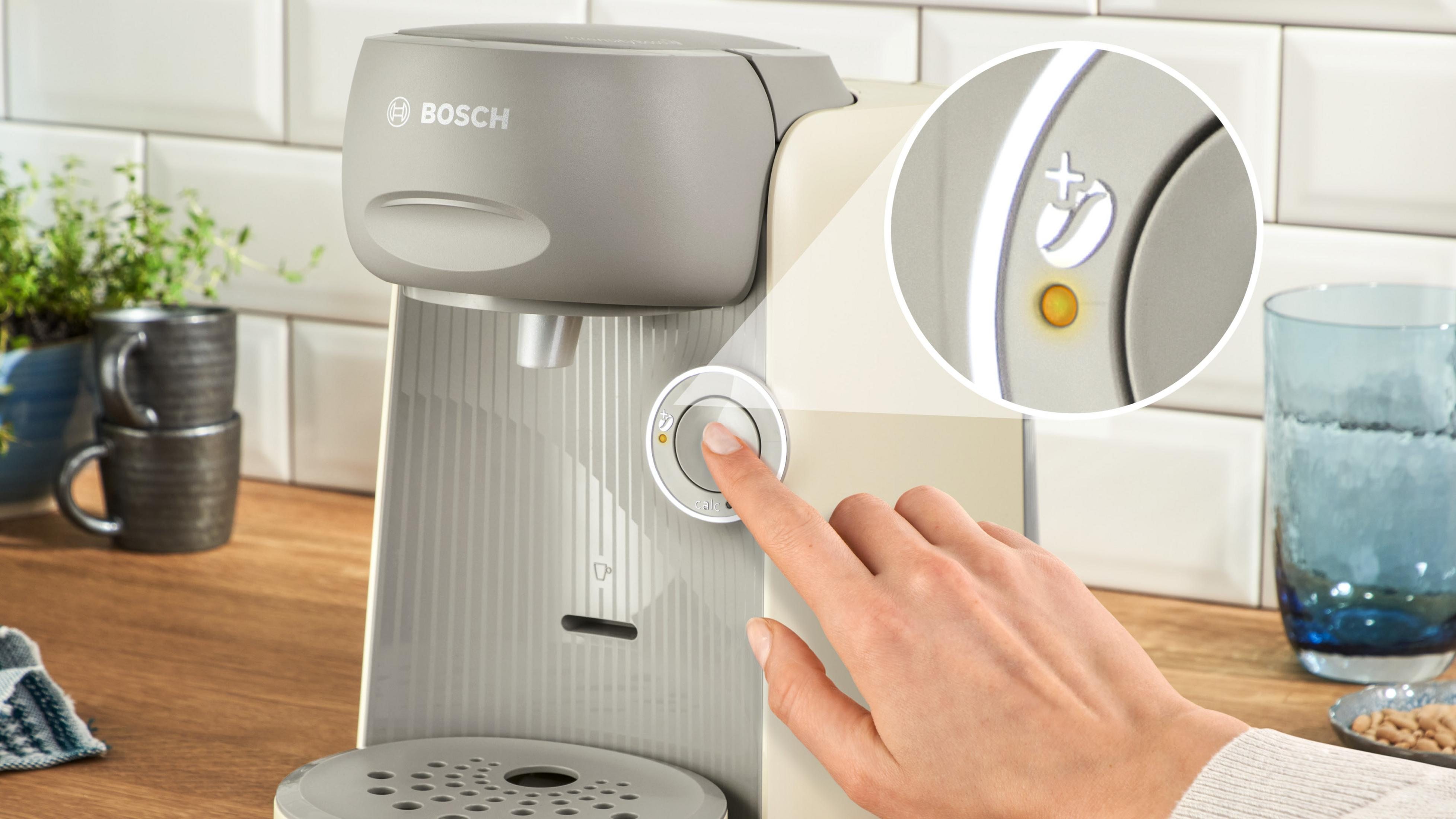 Una mano preme il pulsante di avvio di una macchina da caffè Bosch Tassimo beige.