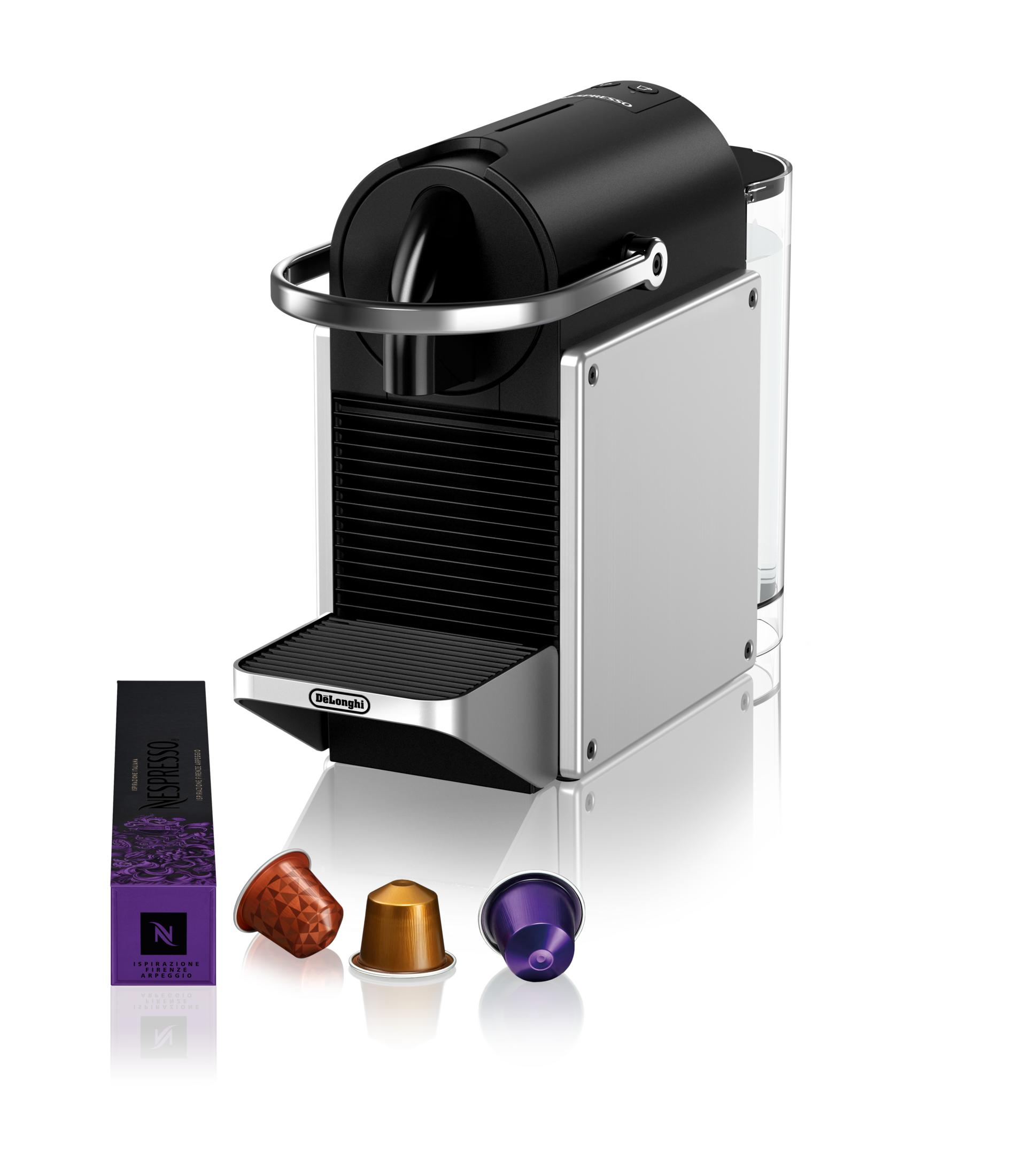 Una macchina da caffè DeLonghi nera e argento con un astuccio di caffè e tre capsule su superficie bianca.
