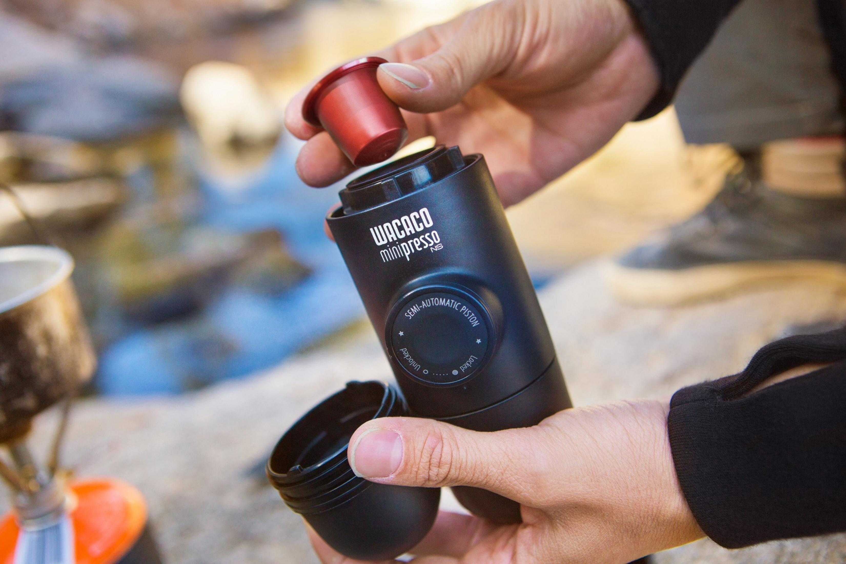 Mains tenant une cafetière noire Wacaco Minipresso et insérant une capsule rouge.