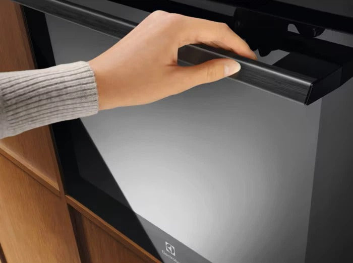 Una persona apre la porta di un moderno forno nero con una maniglia in metallo.