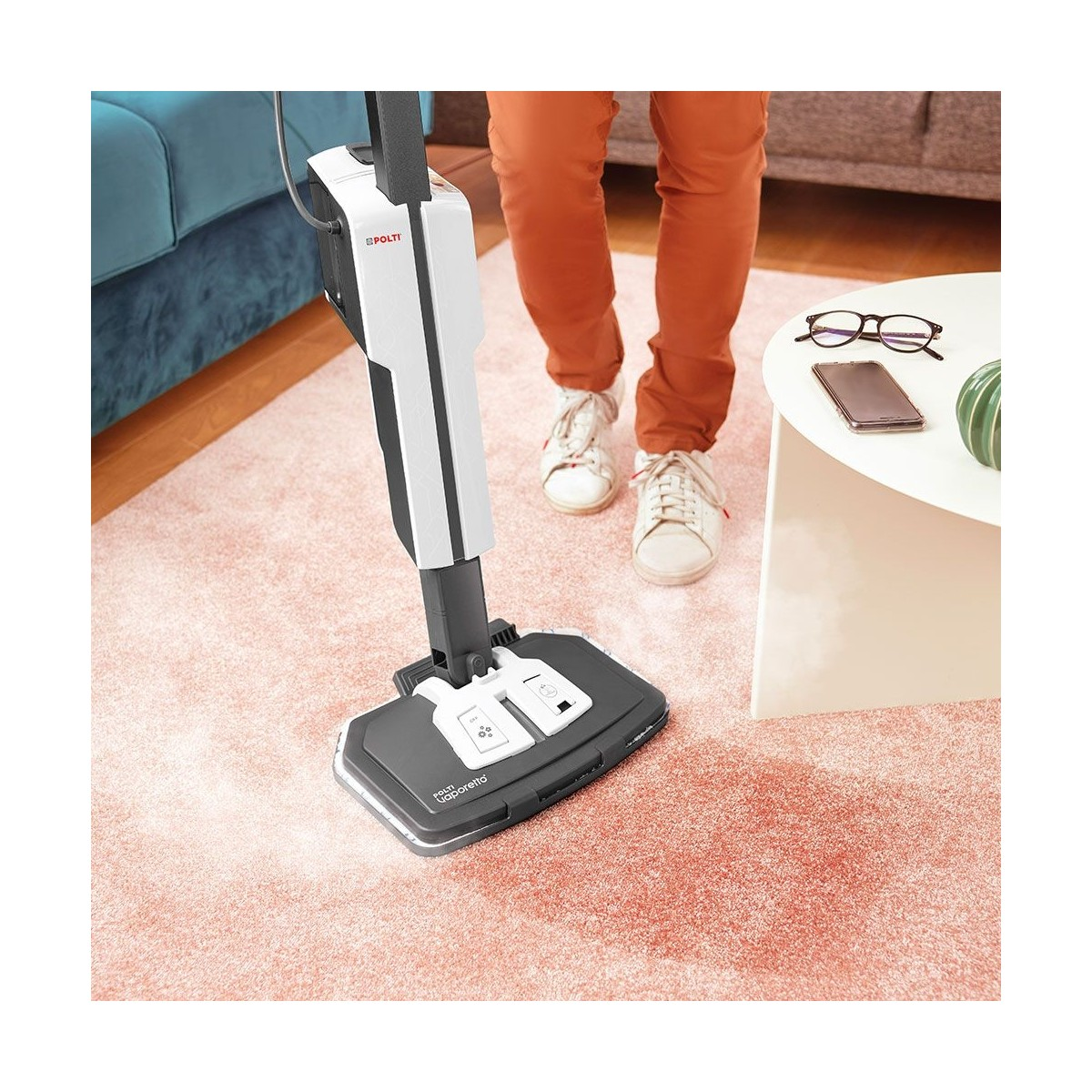 Eine Person benutzt einen weißen Dampfmopp auf einem rosa Teppich in einem Wohnzimmer.