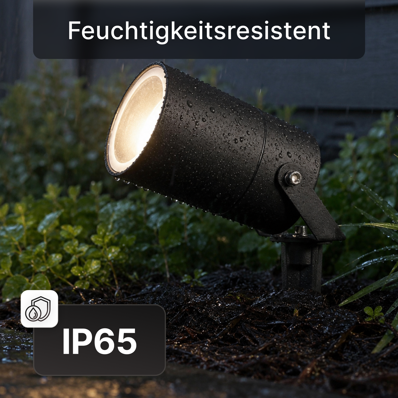 Ein schwarzer, feuchtigkeitsresistenter Gartenstrahler mit Wassertropfen im Garten bei Nacht.
