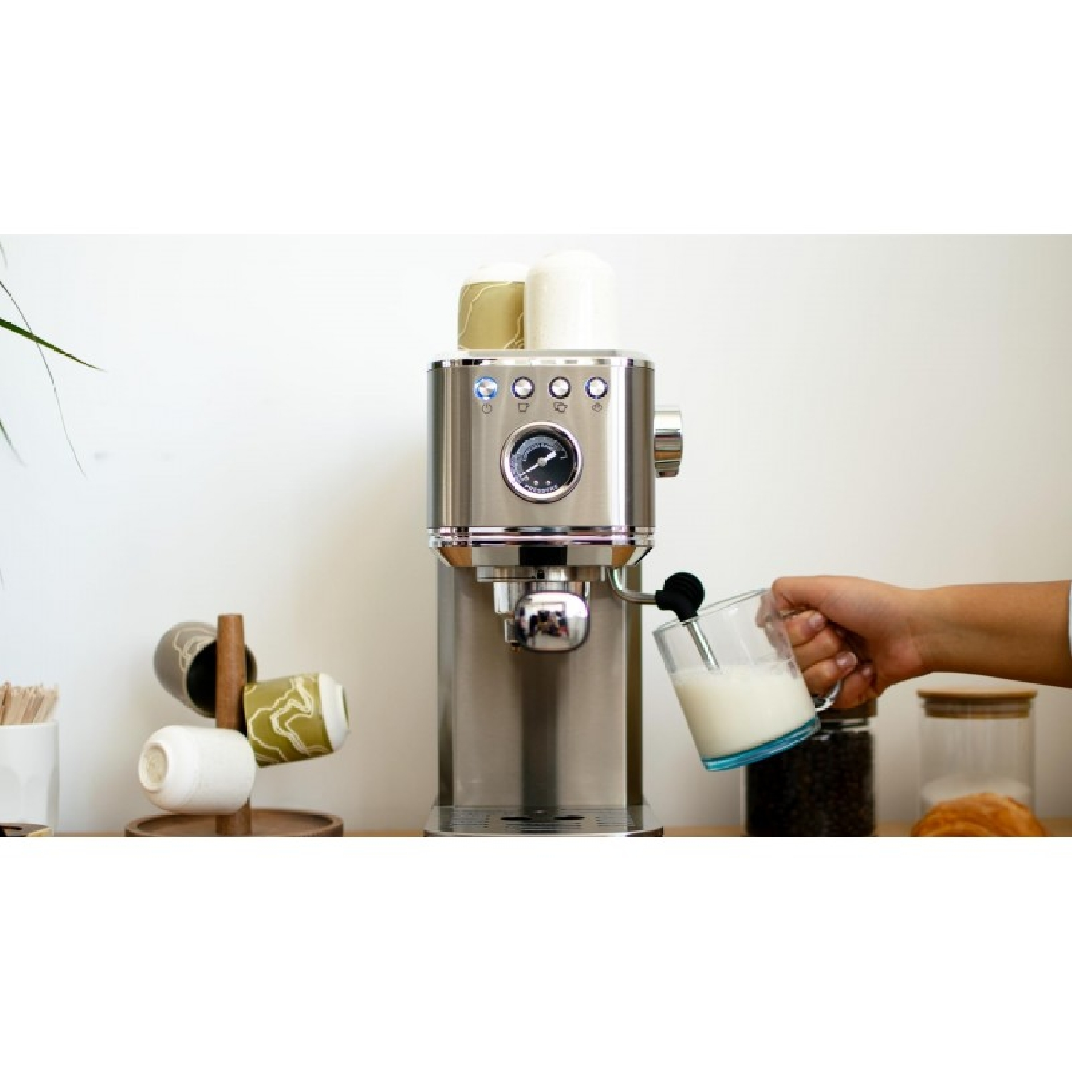 Una mano sostiene un vaso de leche bajo el vaporizador de una cafetera de acero inoxidable.
