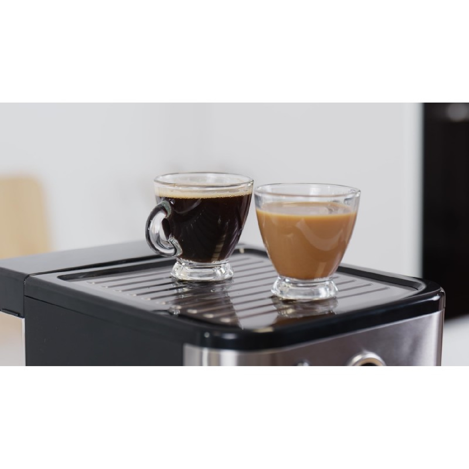 Dos tazas de cristal con café están sobre la bandeja de goteo de una cafetera.