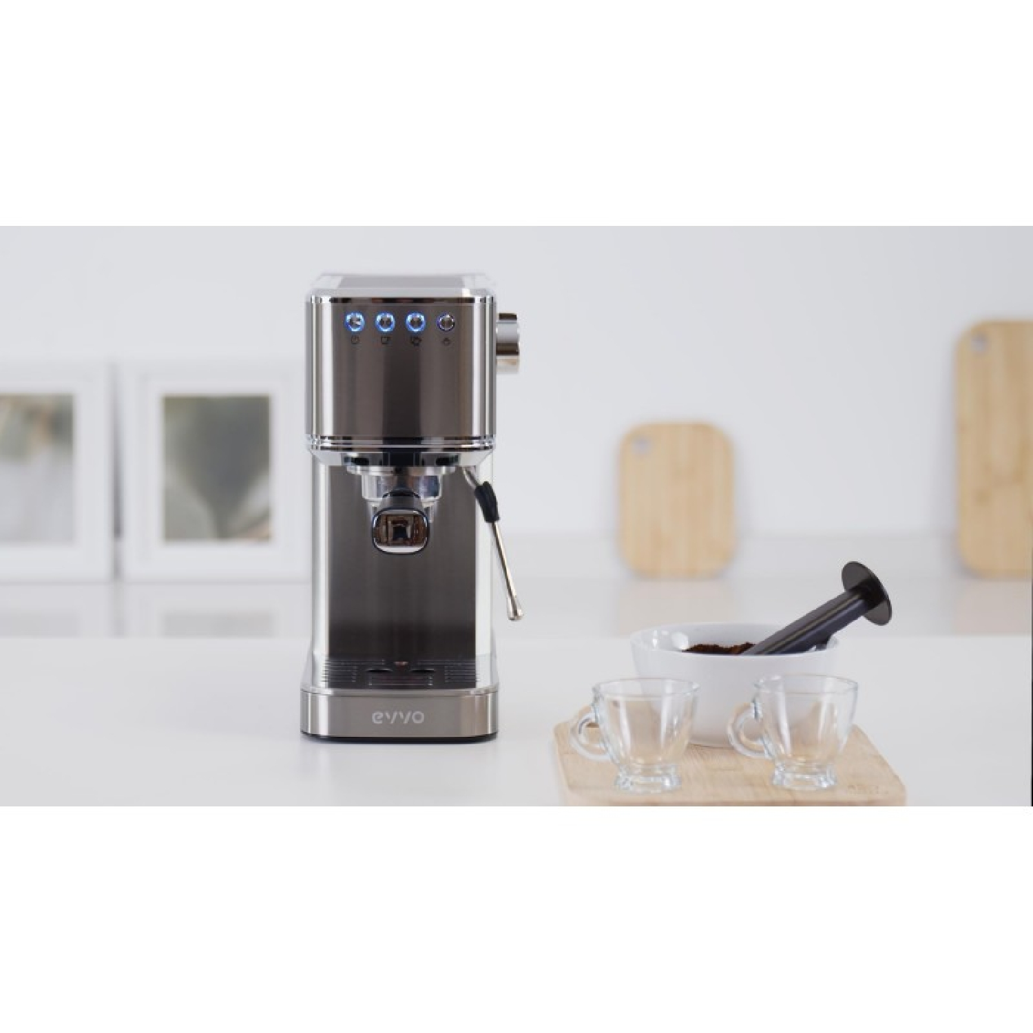 Una cafetera plateada está en una encimera junto a dos tazas de vidrio y café molido.