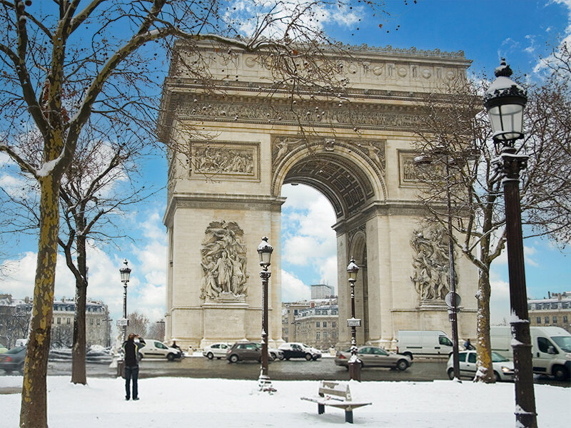 Arco del Triunfo nevado en París con coches en la calle y árboles con escarcha en primer plano.