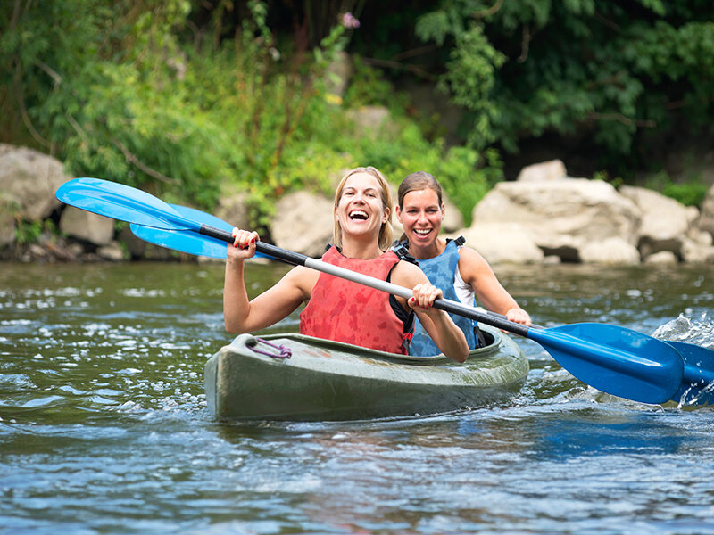 Dos mujeres felices remando juntas en un kayak verde en un río.