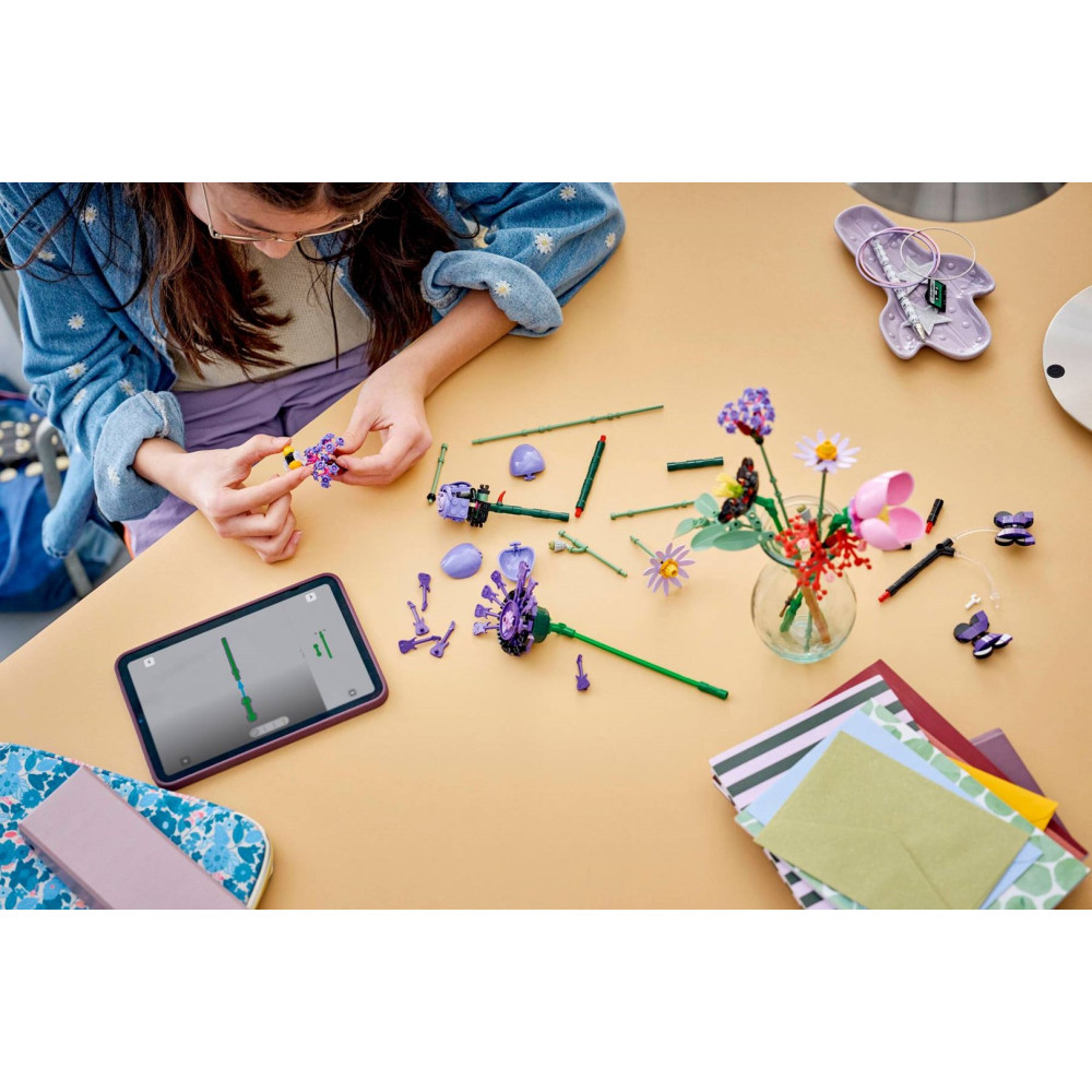 Dziewczynka siedzi przy stole i buduje kwiaty LEGO. Tablet pokazuje instrukcje.