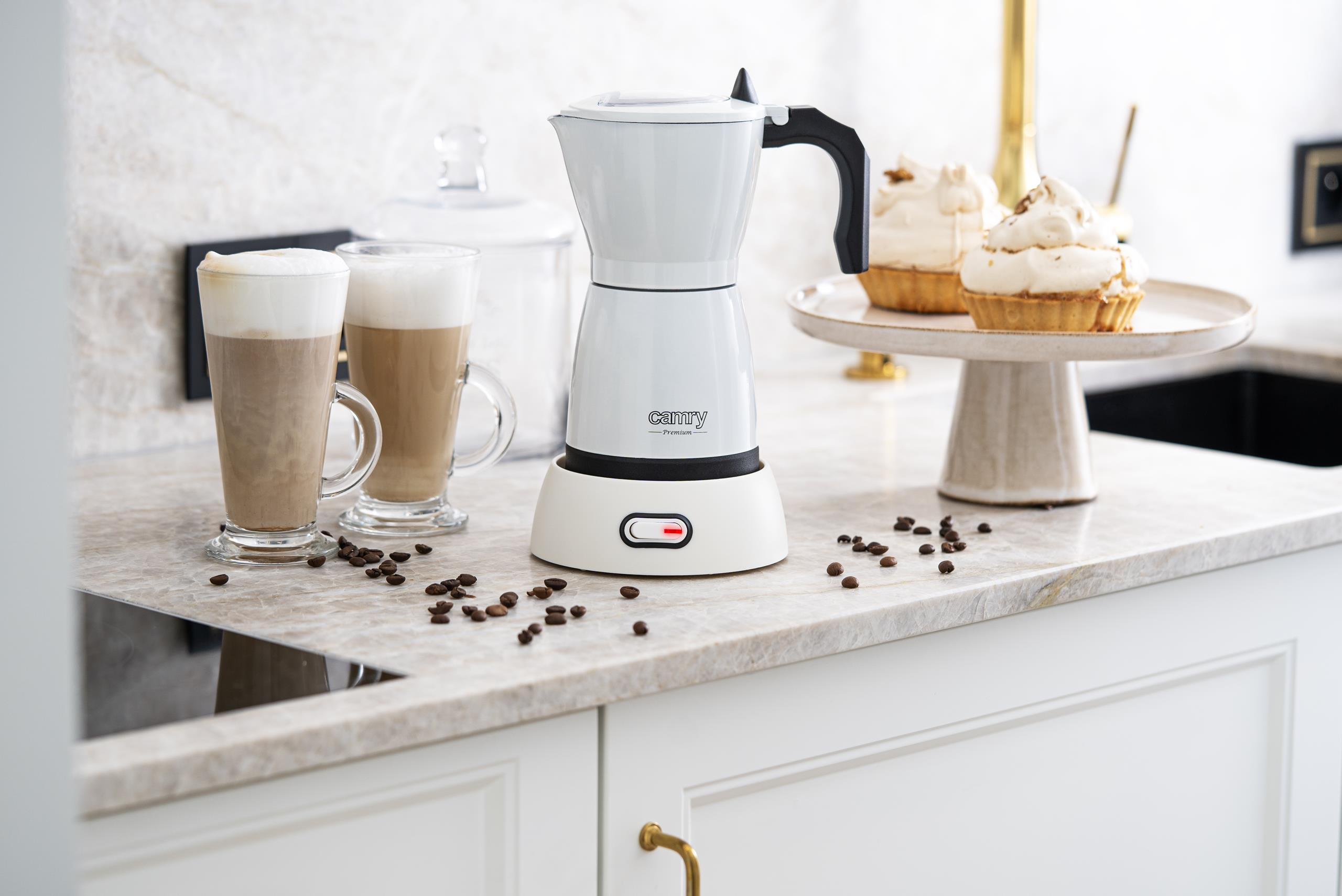 Una caffettiera Camry bianca, due bicchieri da latte e dolci su un piano di marmo.