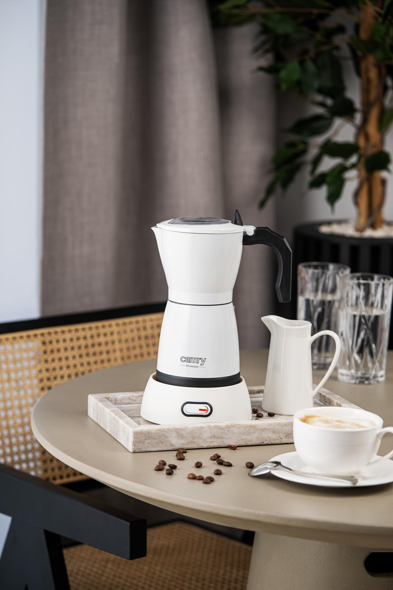Una macchina da caffè espresso Camry bianca su un vassoio con chicchi di caffè e una tazza sul tavolo.