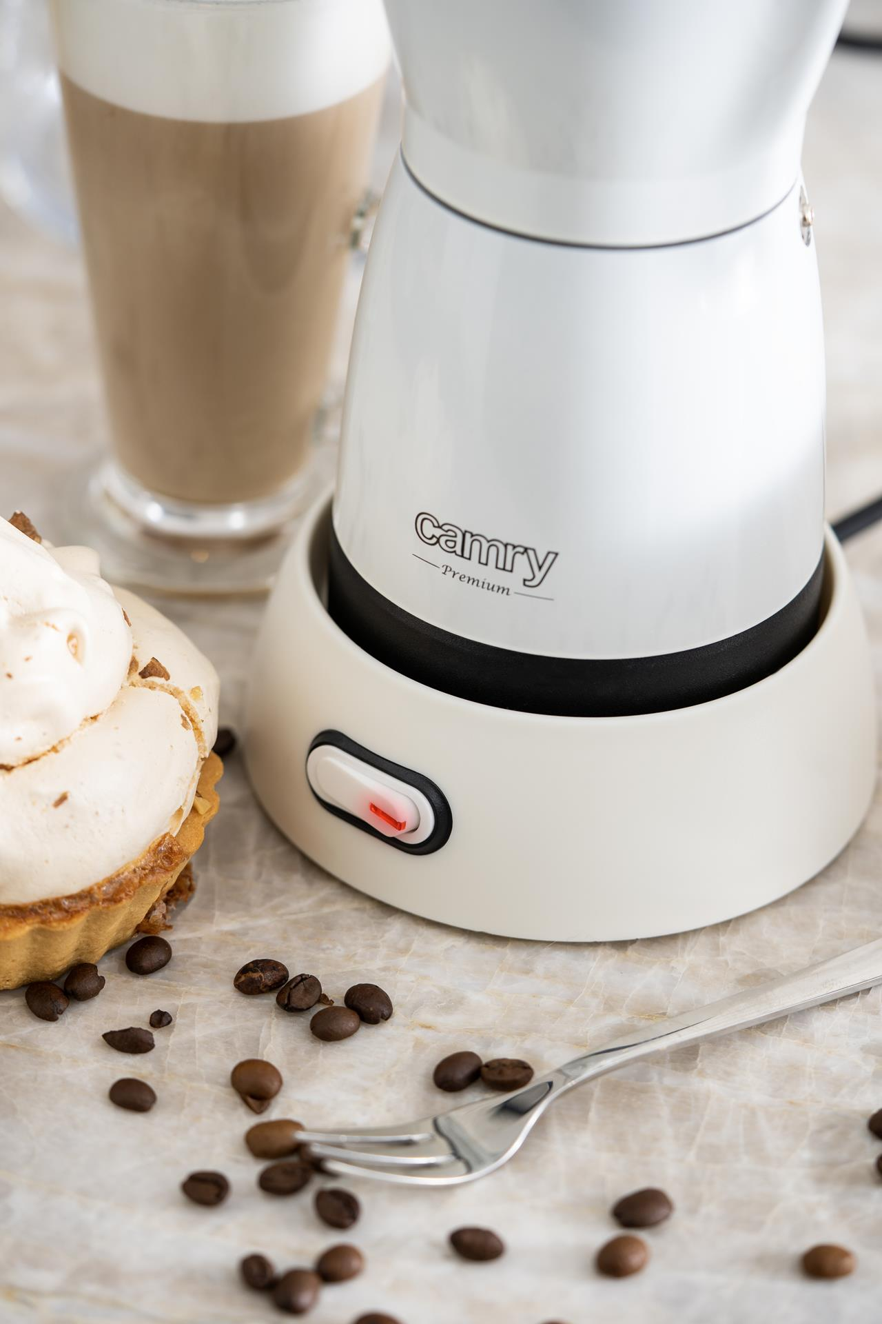 Montalatte Camry bianco su base, circondato da chicchi di caffè, un dolce e un bicchiere di latte macchiato.