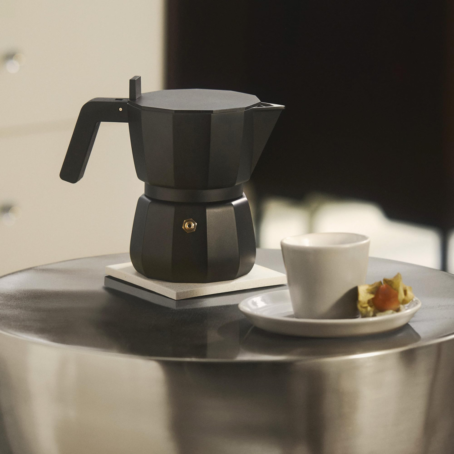 Caffettiera moka nera e tazza bianca su un tavolo argentato.
