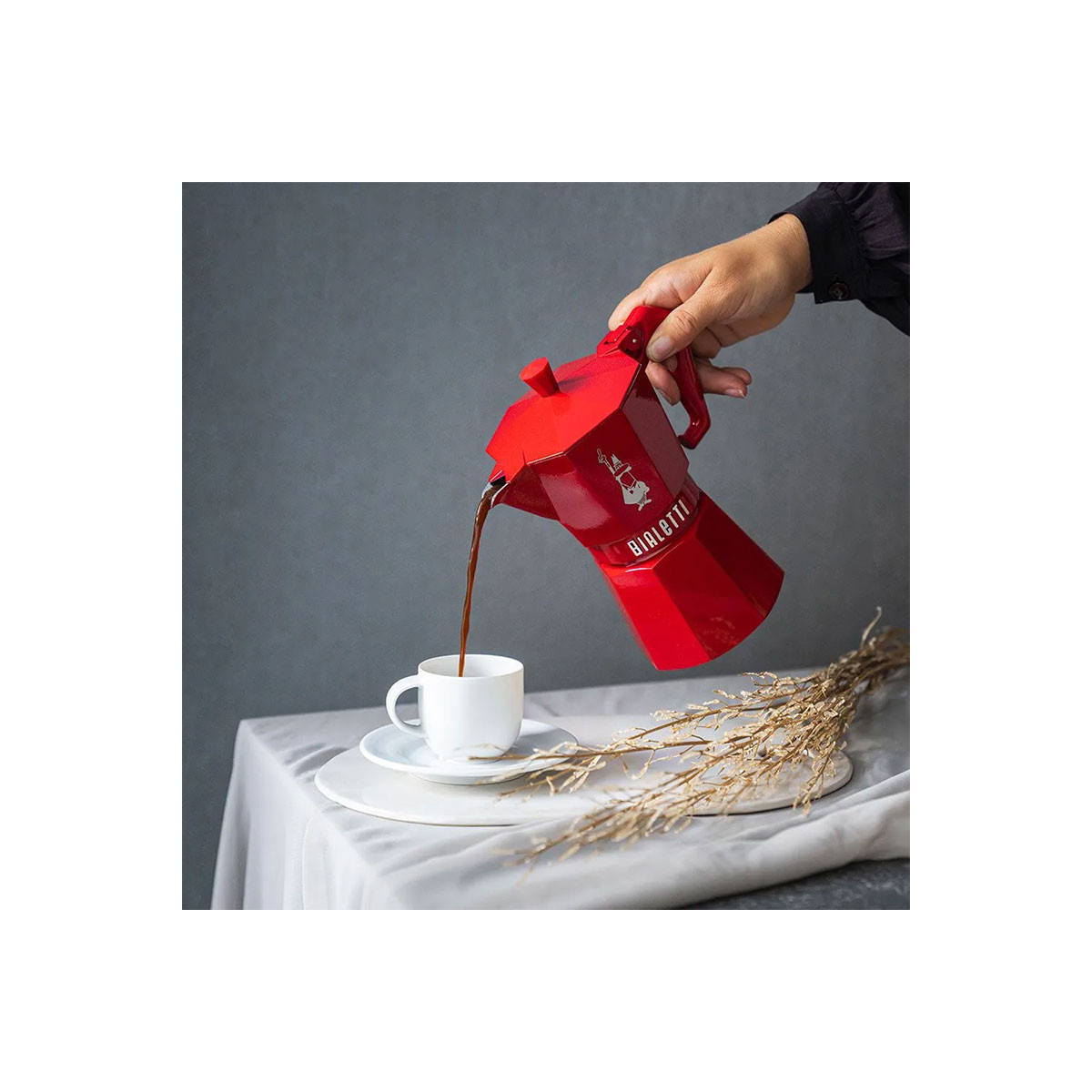 Una mano versa il caffè da una moka rossa in una tazza bianca.