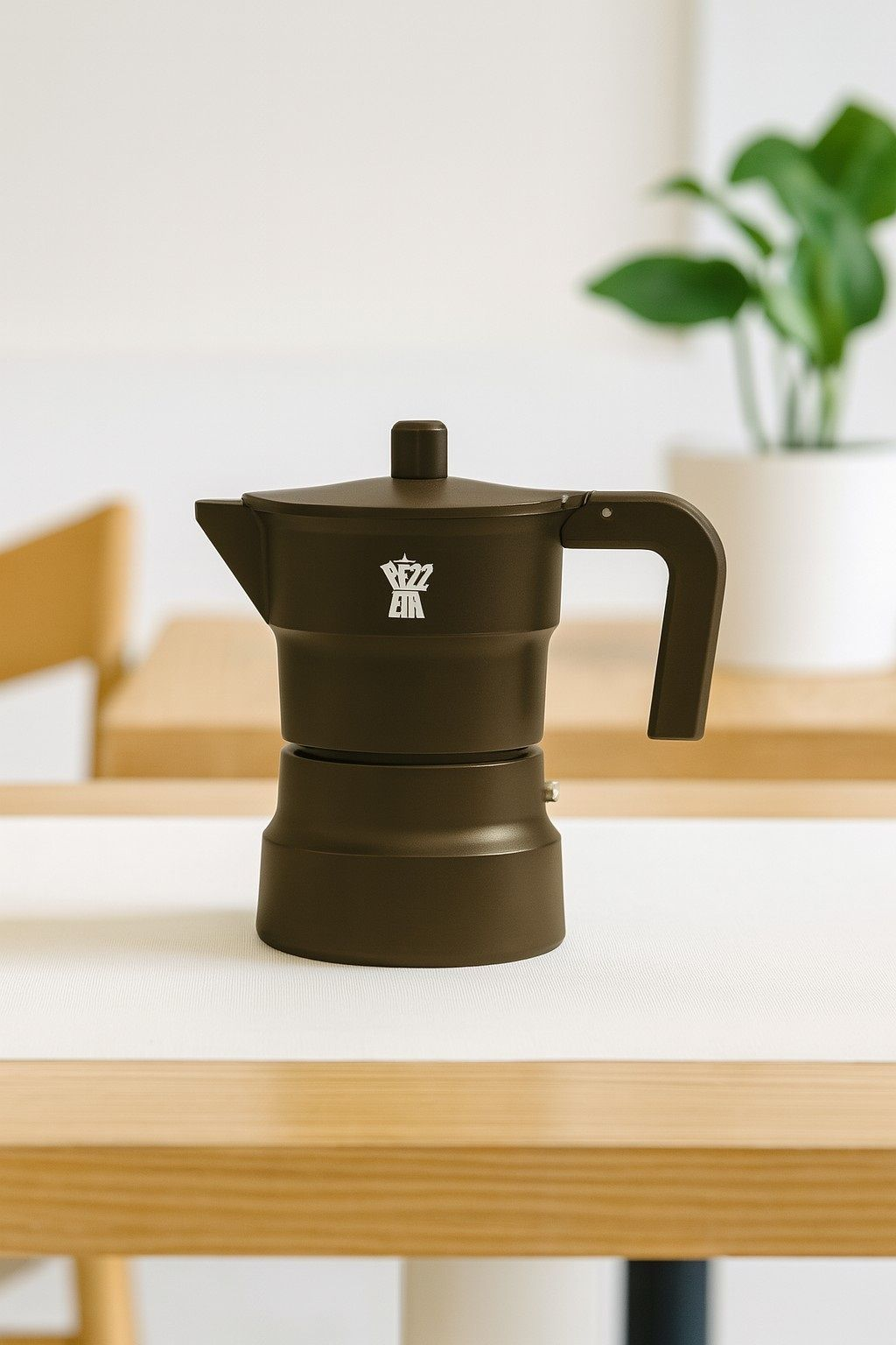 Una moka nera è appoggiata su un tavolo di legno con una pianta in vaso sfocata sullo sfondo.