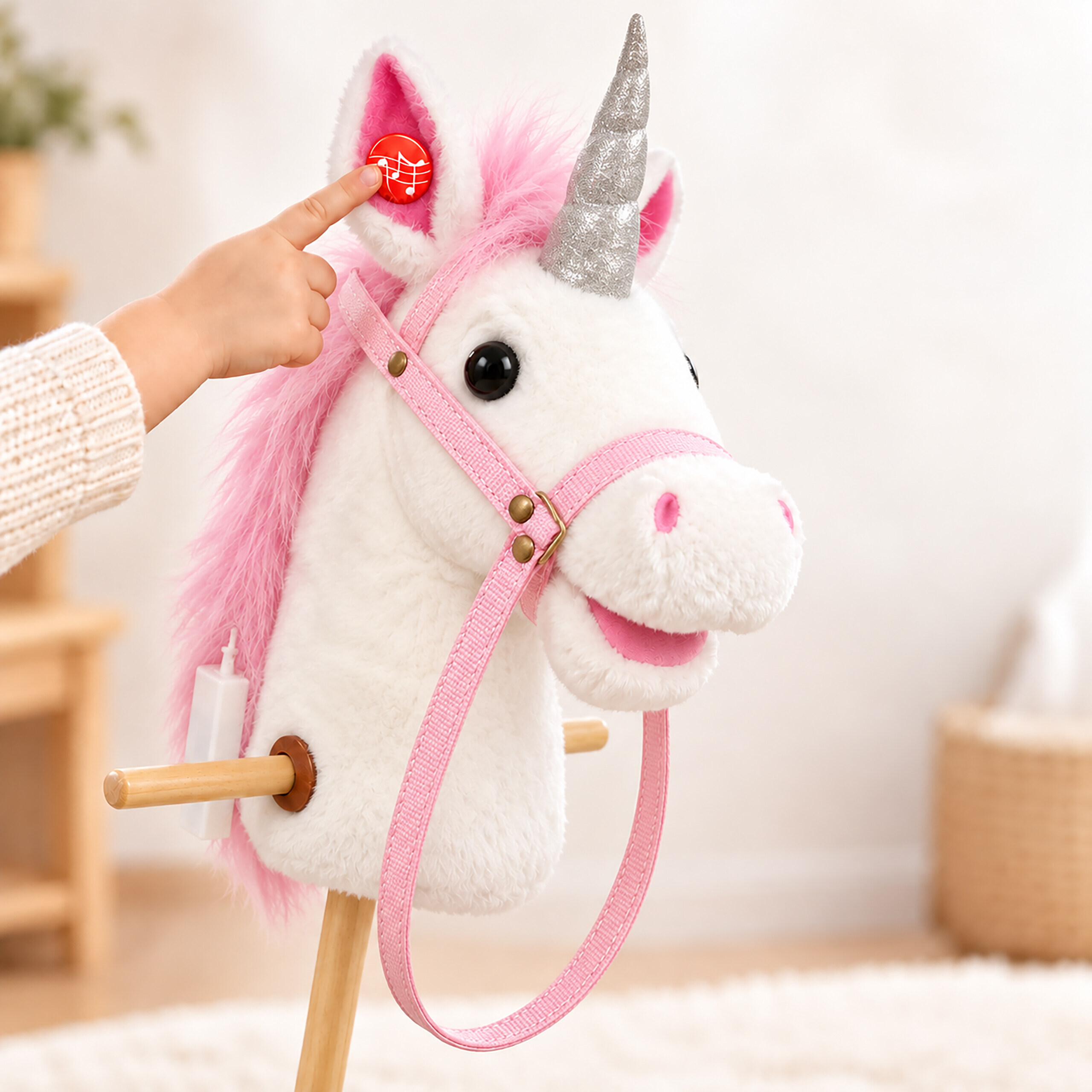 Eine Kinderhand drückt einen roten Musikknopf am Ohr eines weiß-rosa Steckenpferds mit glitzerndem Horn.