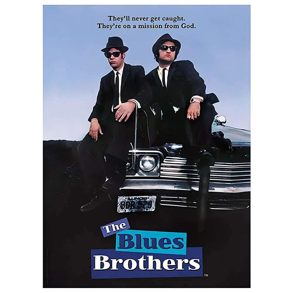 Two men in black suits and hats sit on the hood of a car.