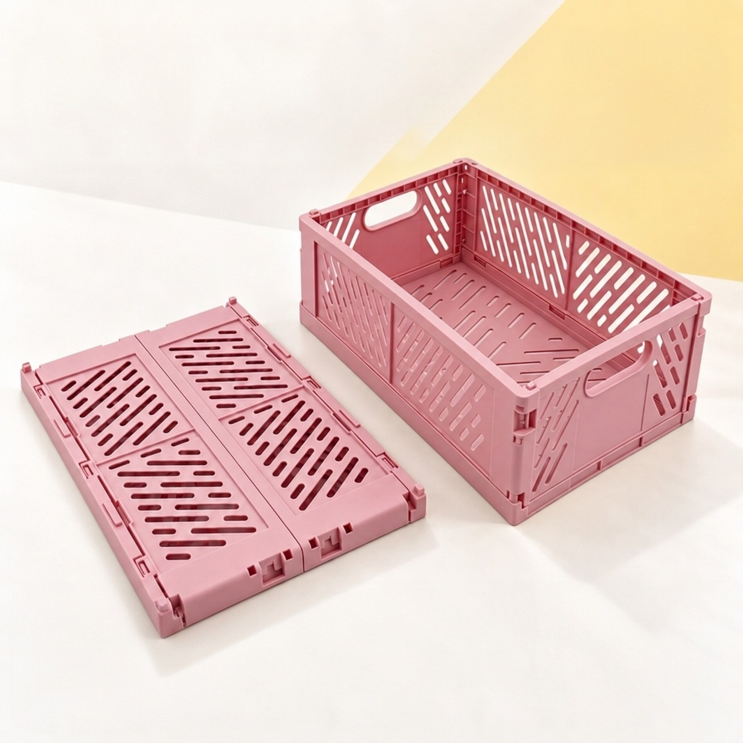 Eine offene rosa Plastikbox und eine zusammengeklappte flache Box auf weiß-gelbem Grund.