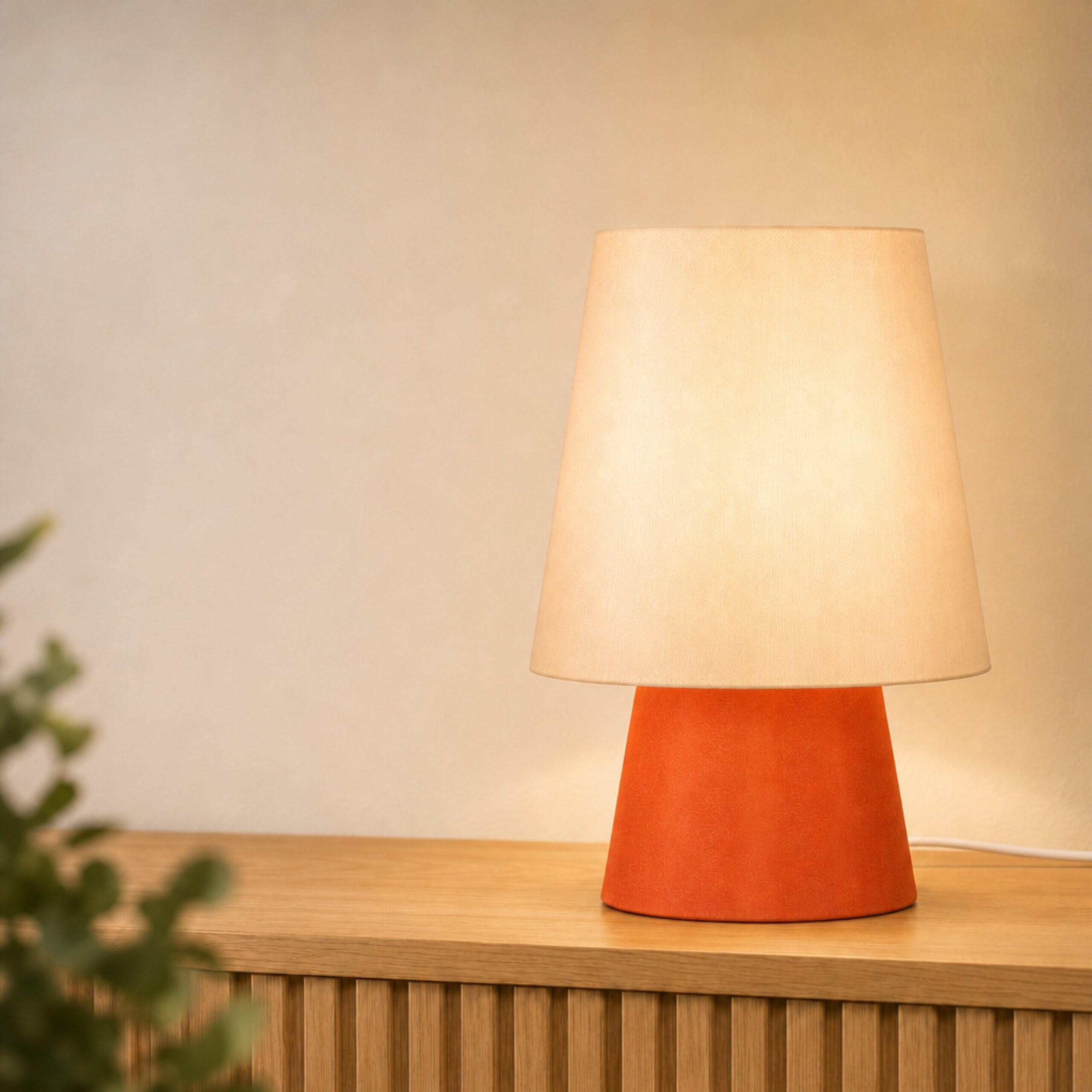 Eine orangefarbene Tischlampe mit einem hellen Lampenschirm steht auf einem Holzschrank.