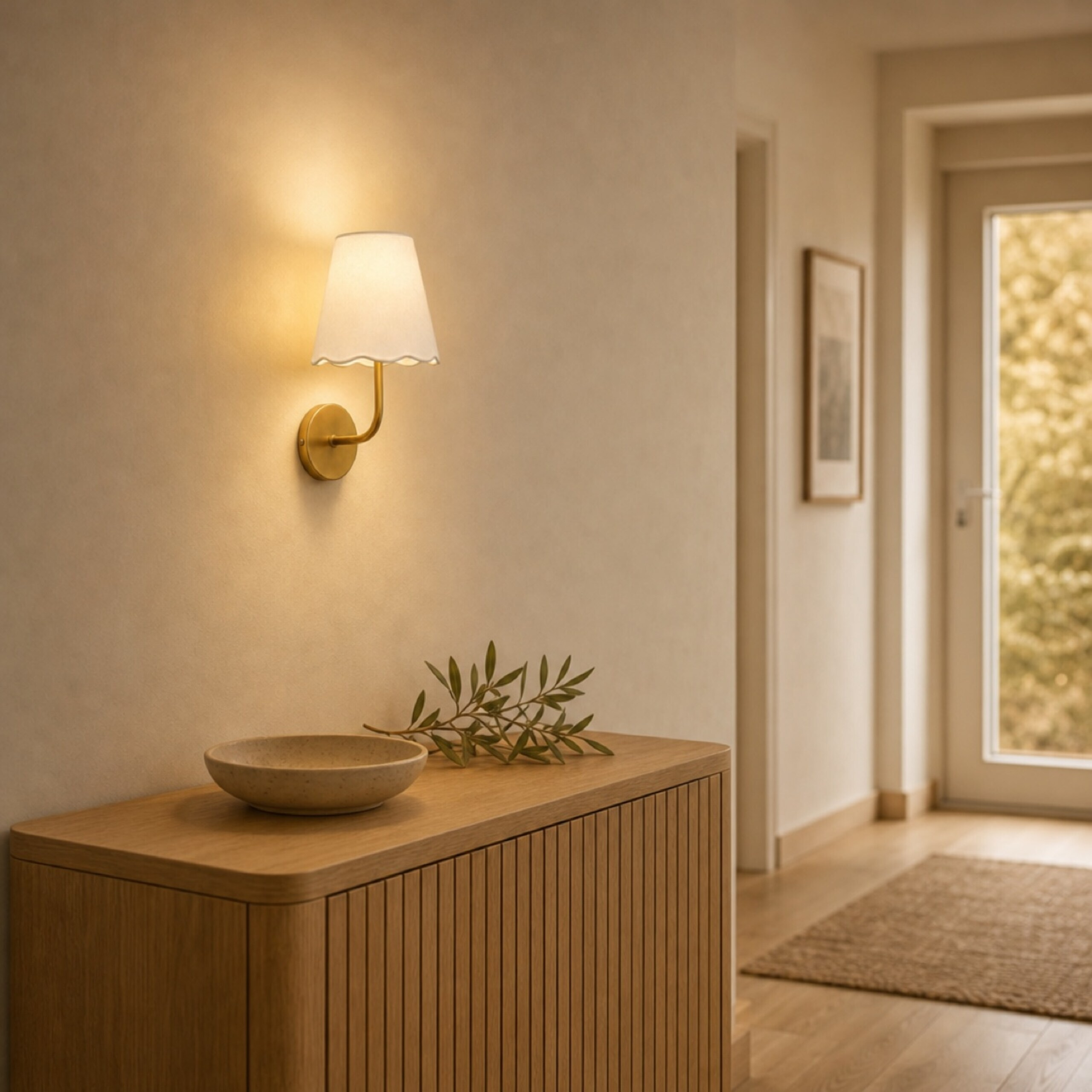 Eine Leuchte an einer Wand beleuchtet einen Holztisch mit einer Schale und Zweigen in einem hellen Flur.