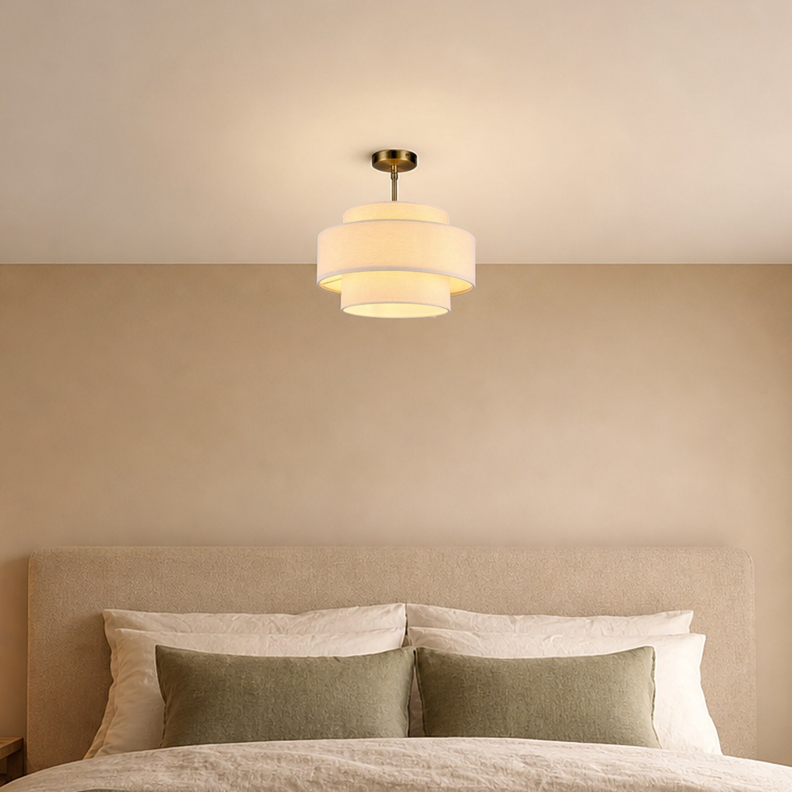 Eine beige Deckenlampe mit drei Schirmen hängt über einem hellen Bett mit grünen Kissen.