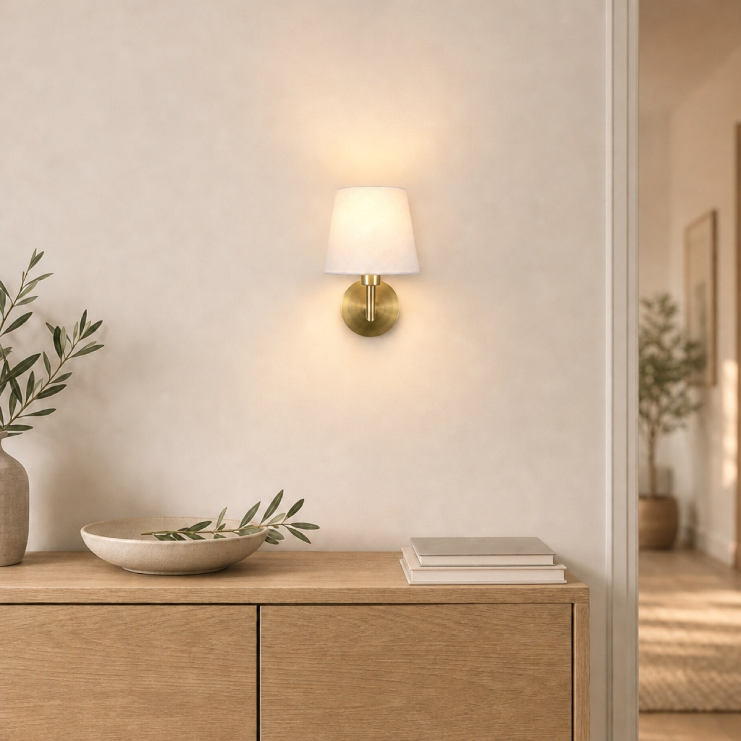 Eine goldene Wandleuchte mit weißem Schirm leuchtet über einer Holztruhe mit Büchern und einer Schale.