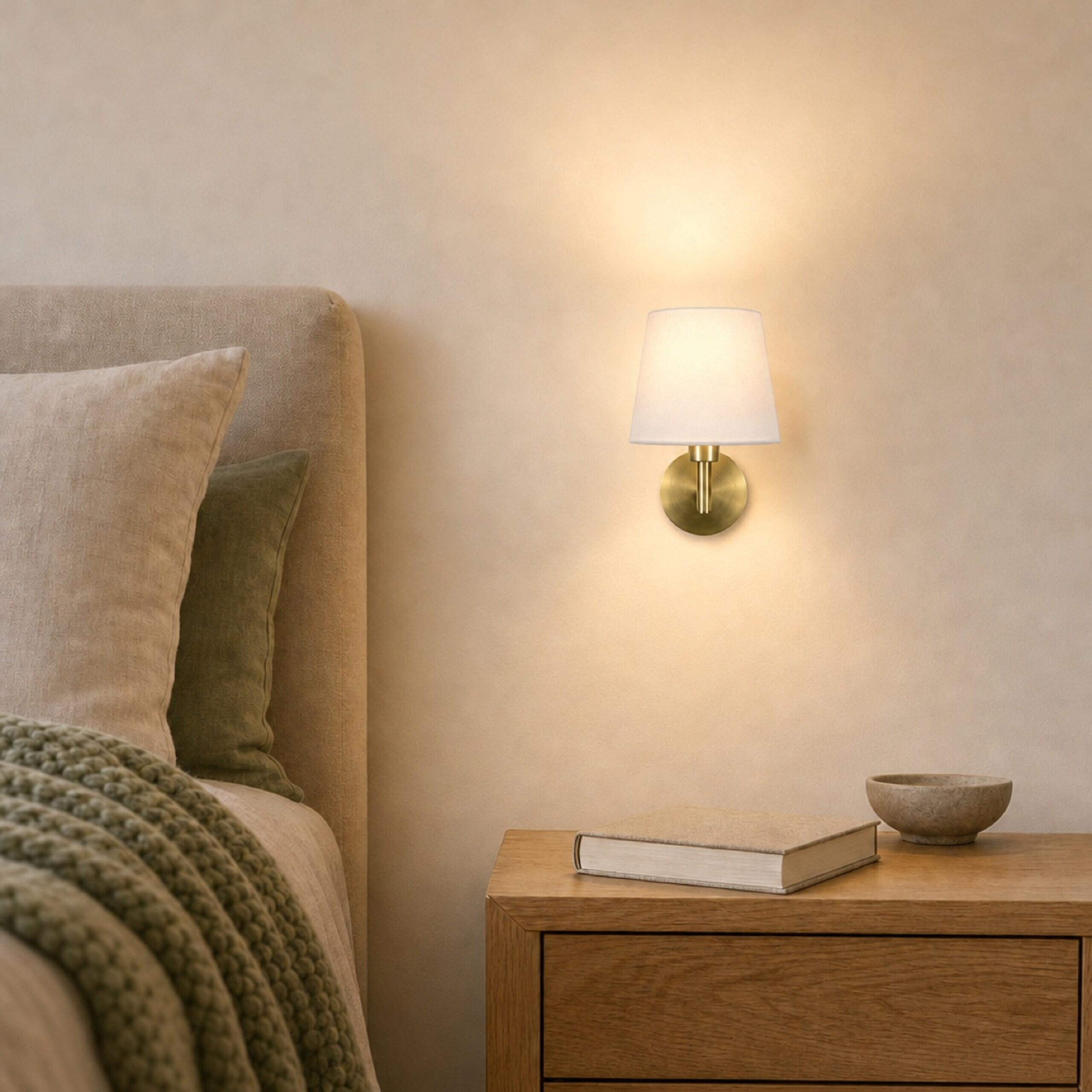 Eine Bettwandlampe mit weißem Schirm leuchtet über einem Nachttisch mit einem Buch und einer Schale.