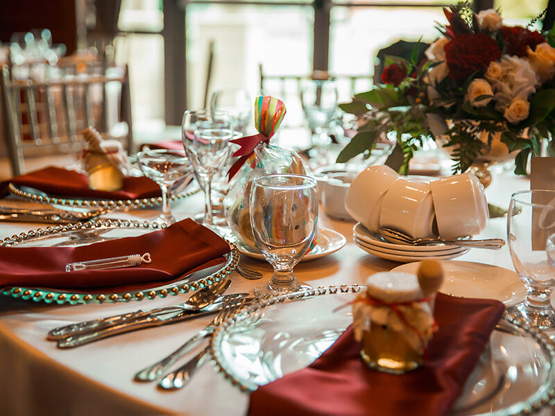 Mesa festivamente puesta con platos rojos y blancos, copas, servilletas y flores.