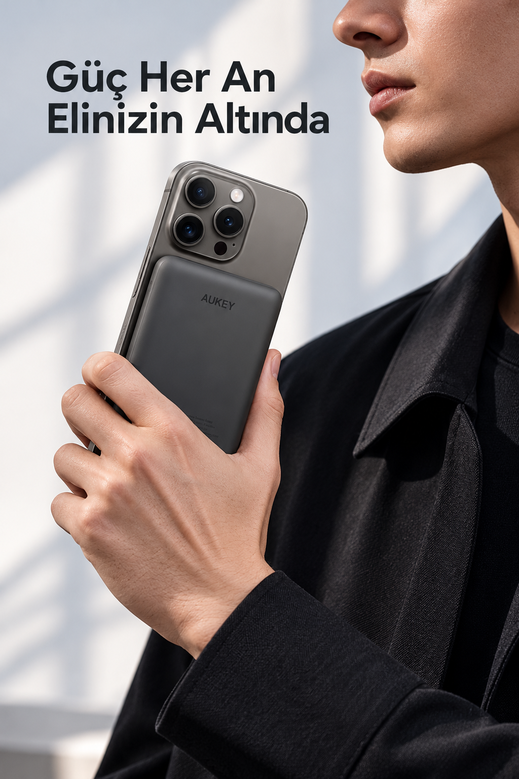 Bir kişi açık arka plan önünde arkasında manyetik Aukey taşınmaz şarj cihazı olan gri bir akıllı telefon tutuyor.