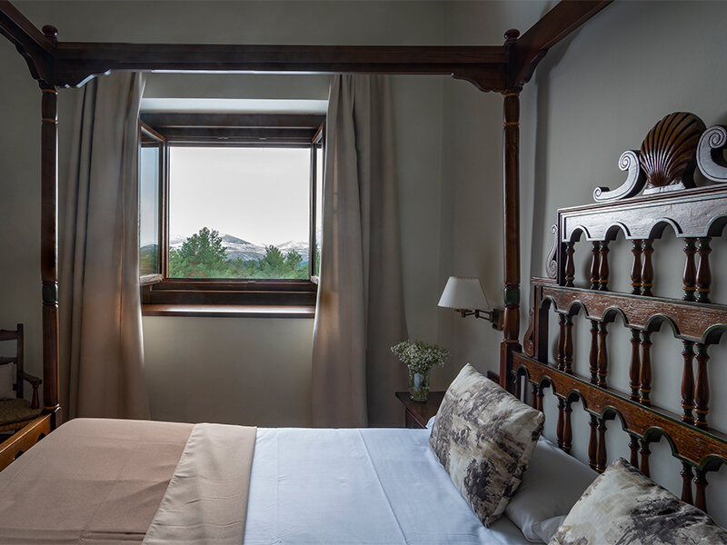 Un dormitorio acogedor con una gran cama de madera con dosel y una ventana con vistas a las montañas nevadas.