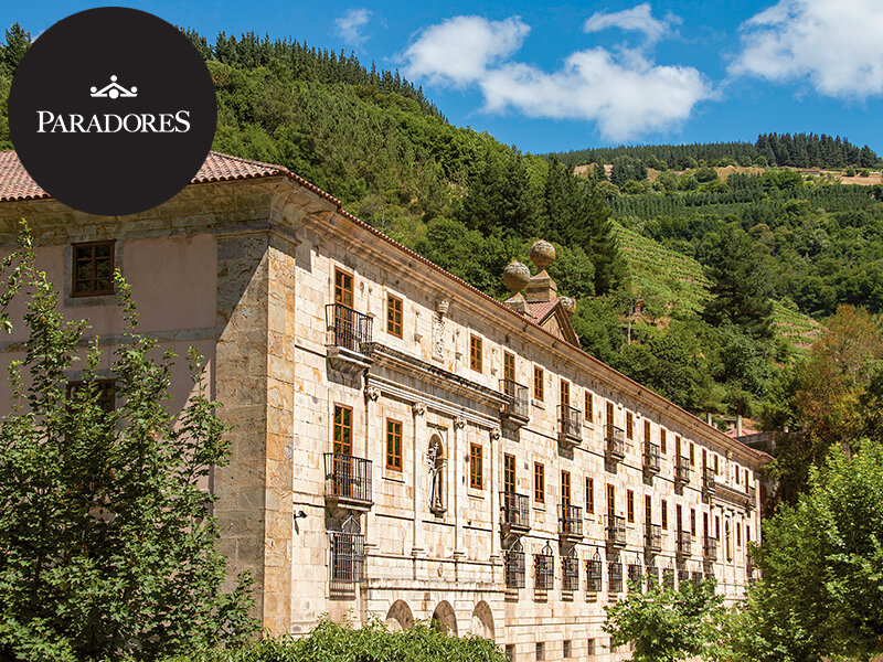 Un gran edificio histórico de piedra con balcones frente a un paisaje verde de colinas.