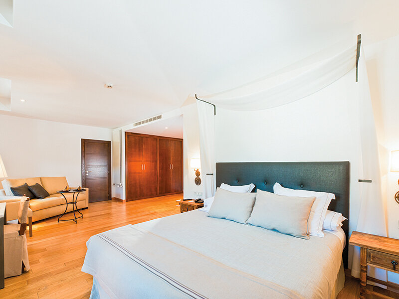 Lujosa habitación de hotel con cama con dosel, suelo de madera y zona de estar con sofá al fondo.