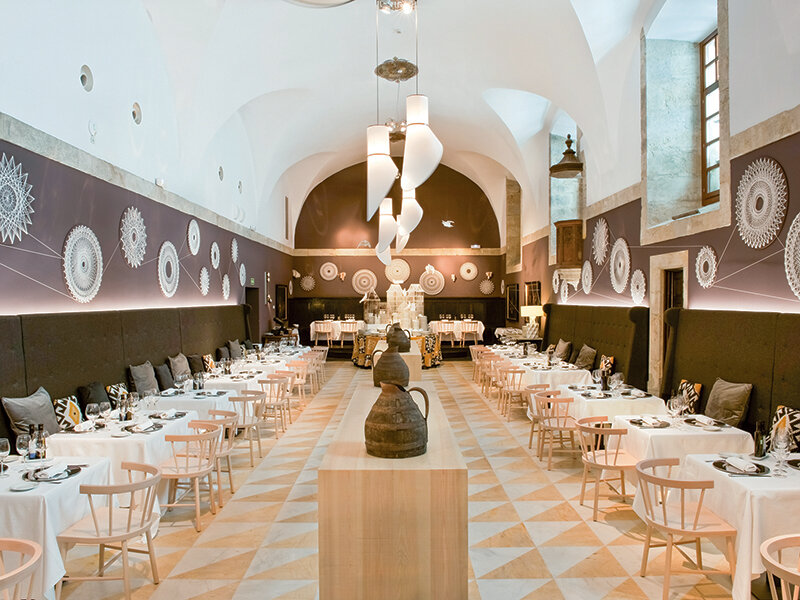 Un interior de restaurante largo con mesas vestidas de blanco, techos abovedados altos y arte de pared decorativo.