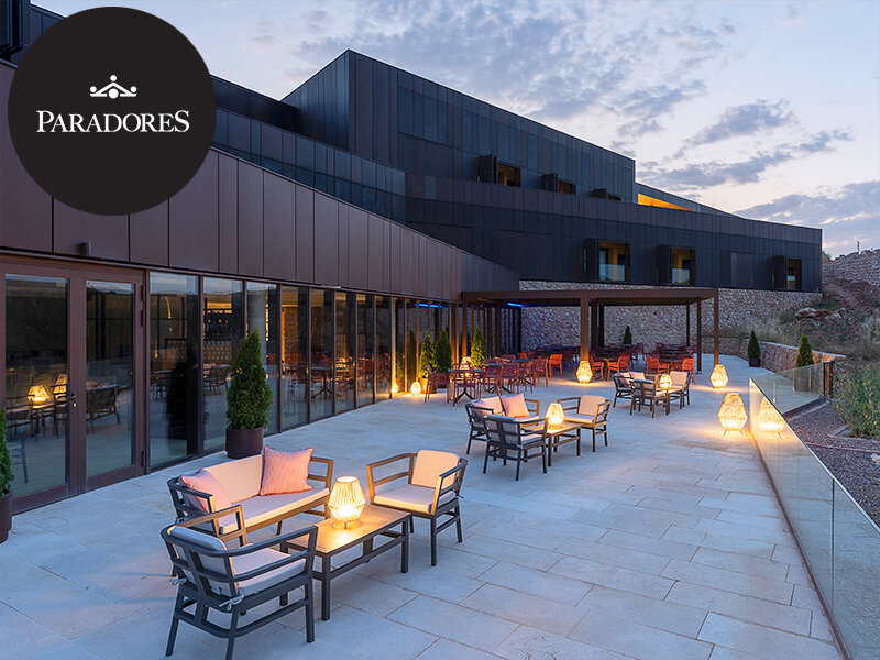 Terraza de hotel moderna al atardecer con muebles iluminados y fachada de cristal.