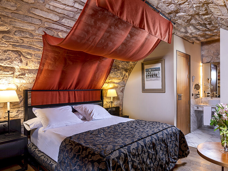 Acogedora habitación con pared de piedra, dosel rojo sobre la cama y baño contiguo.