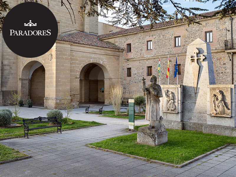 Patio histórico con estatua de piedra, monumento y edificio al fondo.