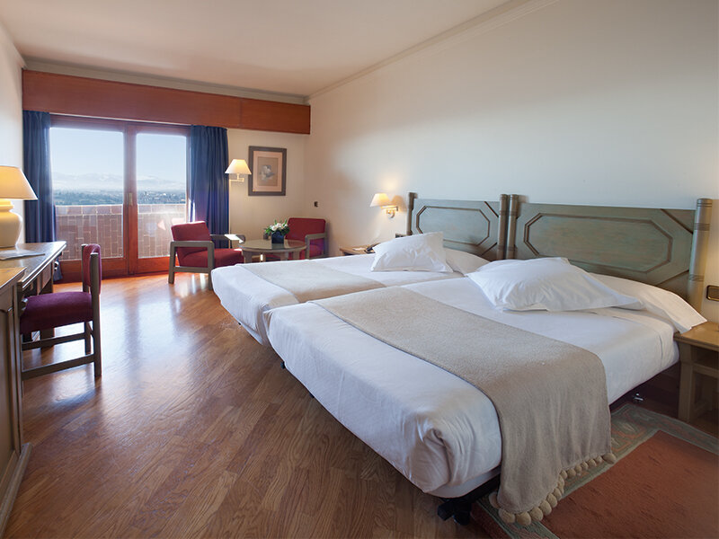 Una habitación de hotel con dos camas individuales, suelo de madera, un escritorio y un balcón.