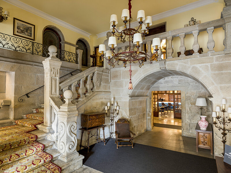 Foyer lujoso con escalera de piedra, gran lámpara de araña y muebles clásicos.